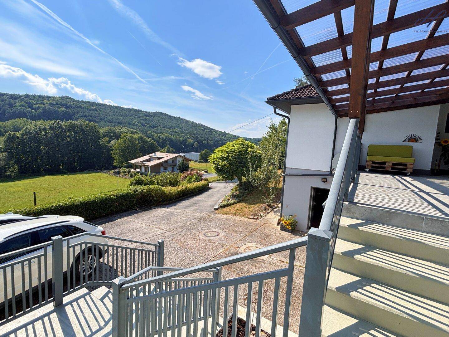 Außenansicht des Hauses mit Treppe zur Terrasse und Zufahrt, umgeben von grüner Natur.