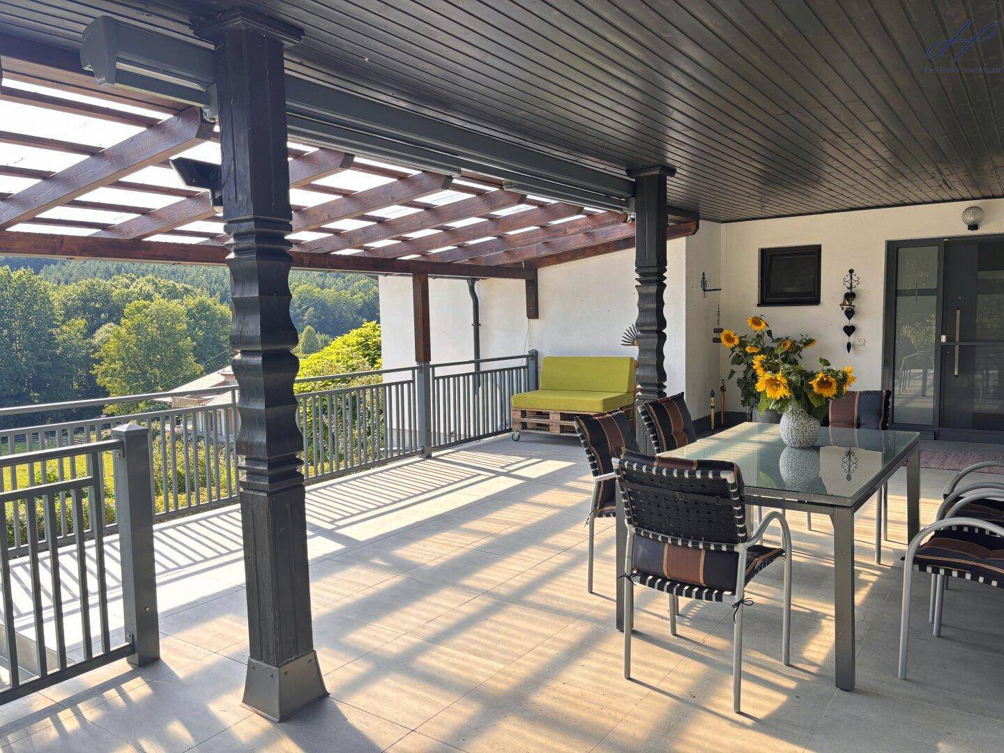 Geräumige, überdachte Terrasse mit Esstisch und Sitzgelegenheiten, bietet weite Aussicht ins Grüne.