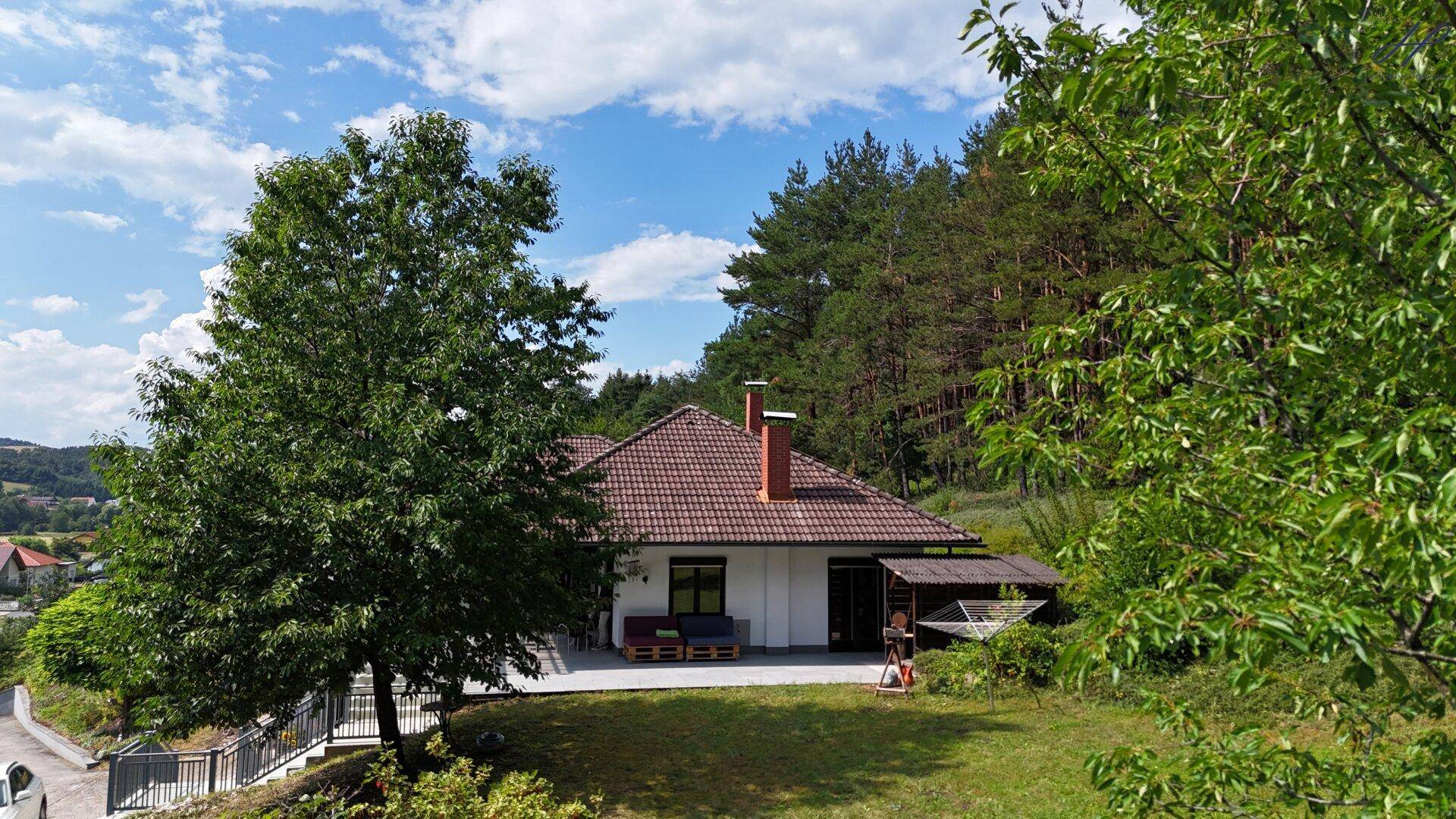 Rückansicht des Hauses mit großer Terrasse und Blick ins Grüne, umgeben von Bäumen.