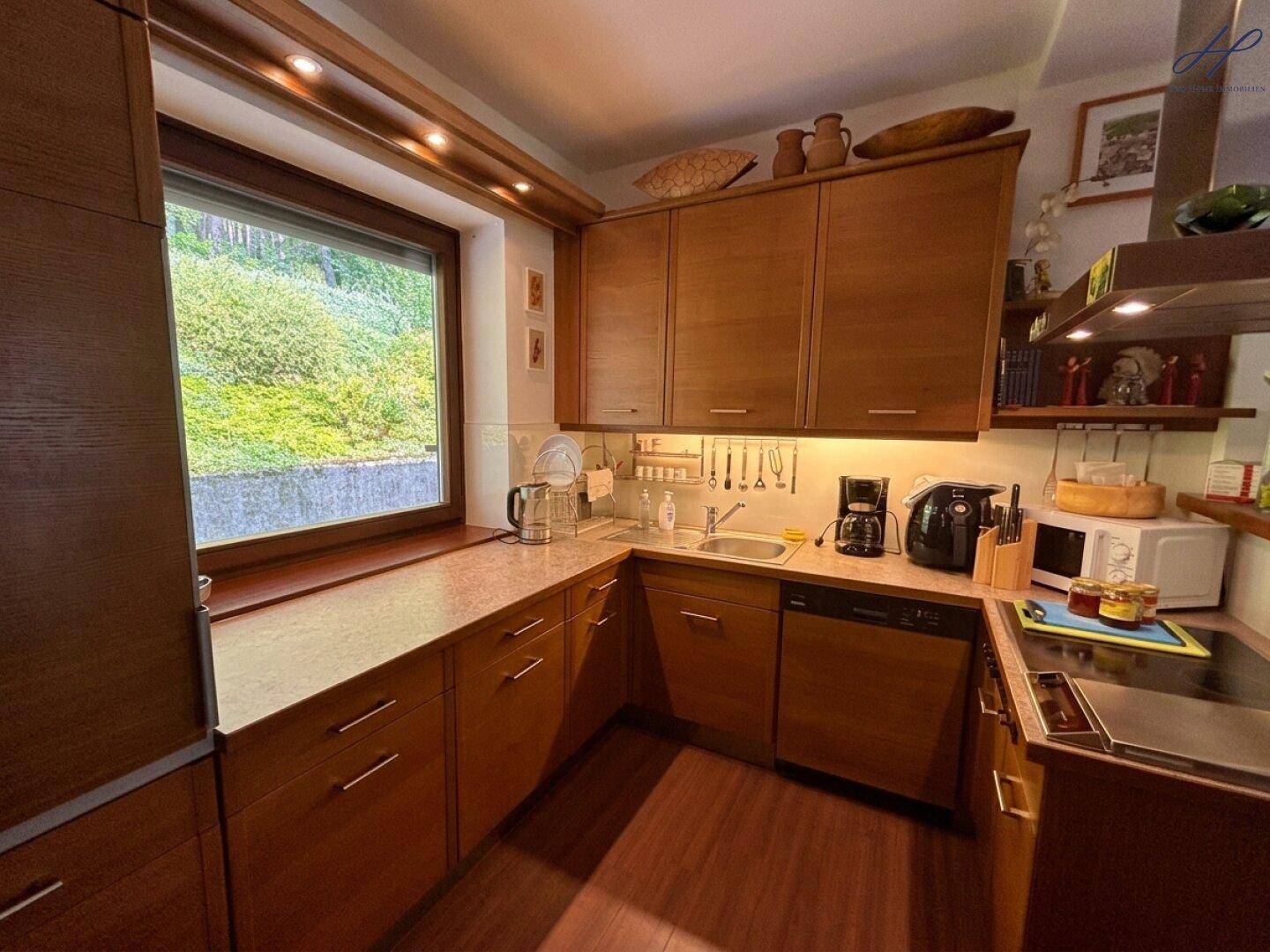 Gut ausgestattete Holzküche mit Fenster, Spüle und Kochfeld, bietet ausreichend Arbeitsfläche.