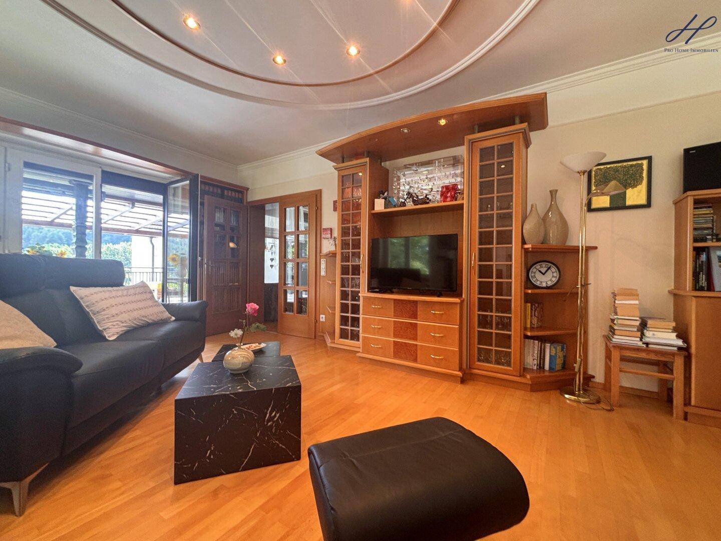 Helles Wohnzimmer mit Zugang zur Terrasse, Parkettboden und umfangreichen Holzregalen.
