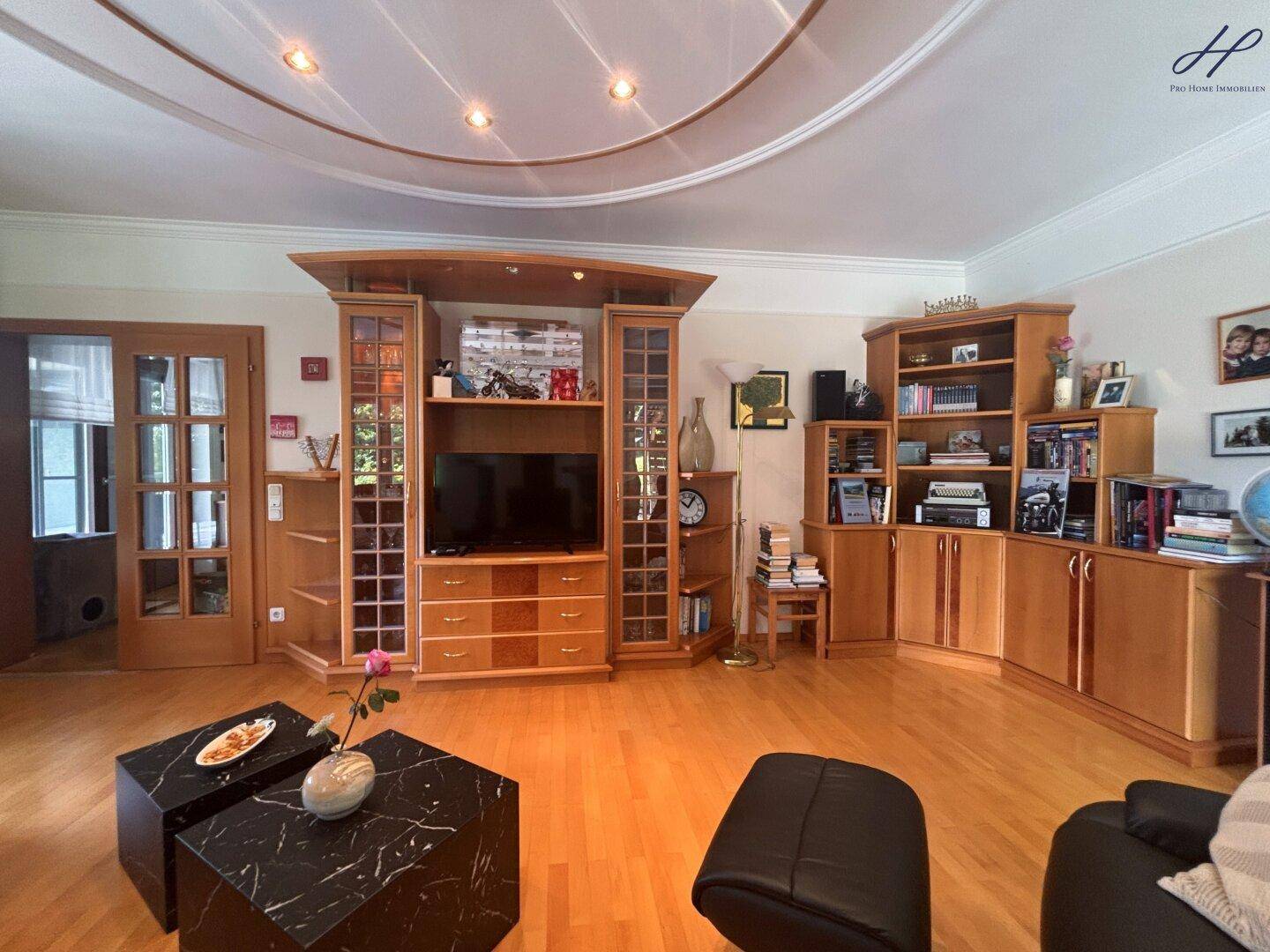 Großzügiges Wohnzimmer mit Parkettboden, Deckenbeleuchtung und vielen Holzschränken.