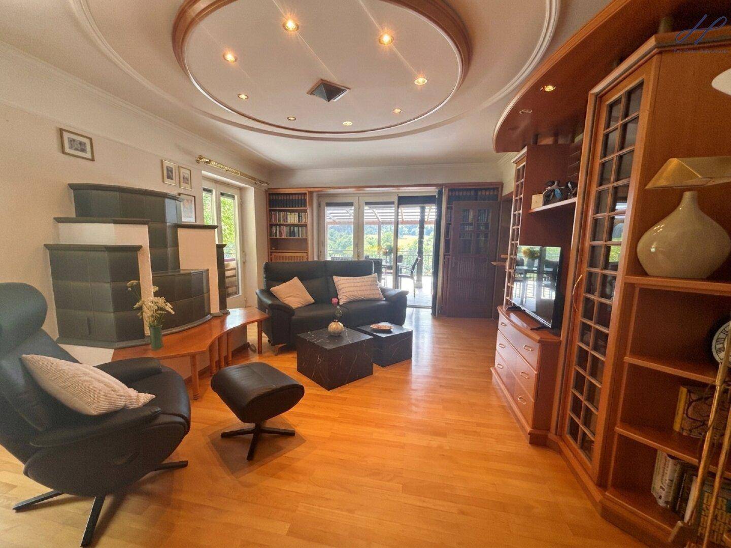 Geräumiges Wohnzimmer mit Holzboden, Kachelofen und Zugang zur Terrasse.