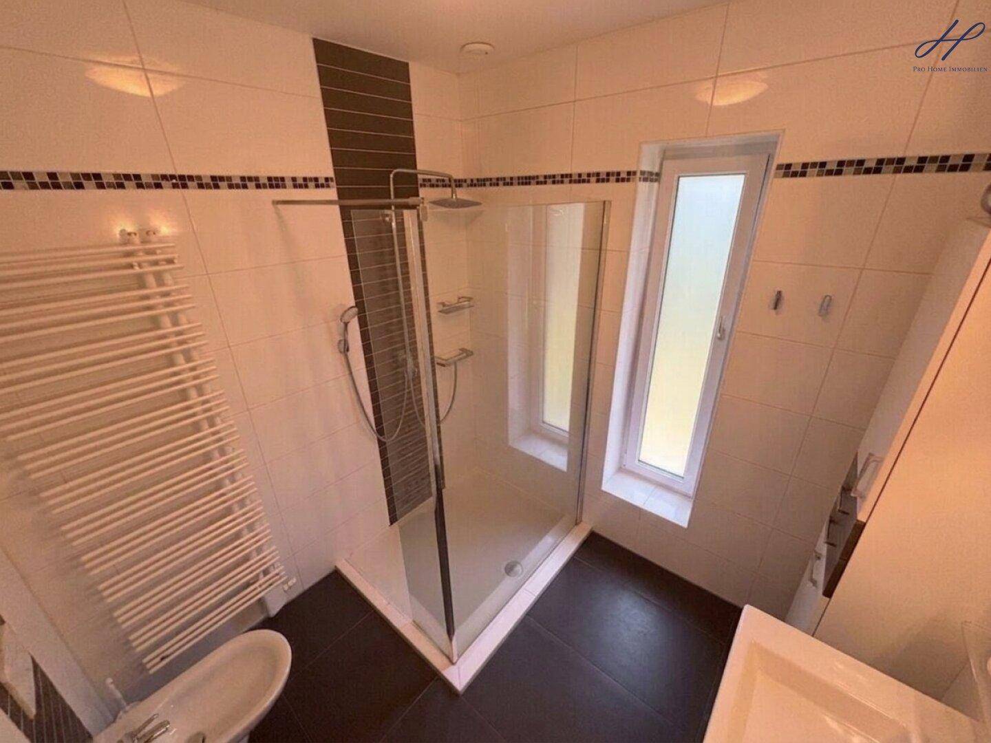 Badezimmer mit großer Duschkabine, Handtuchheizkörper und Fliesenboden.