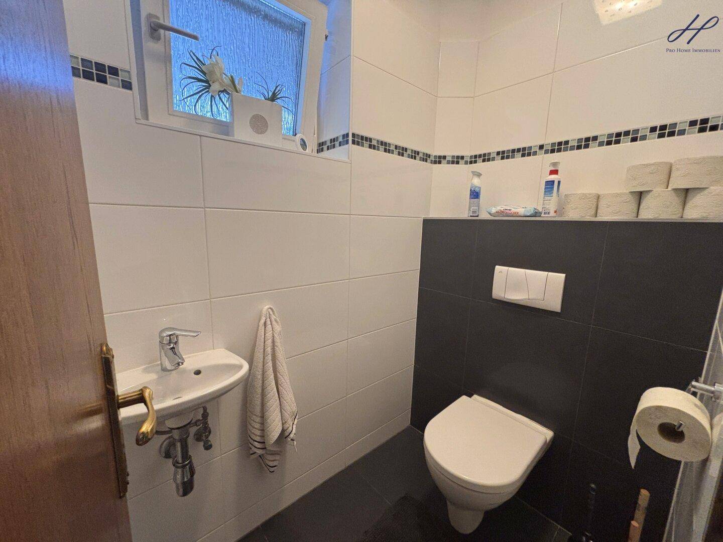 Separate Gästetoilette mit Wand-WC, kleinem Waschbecken und Fenster.