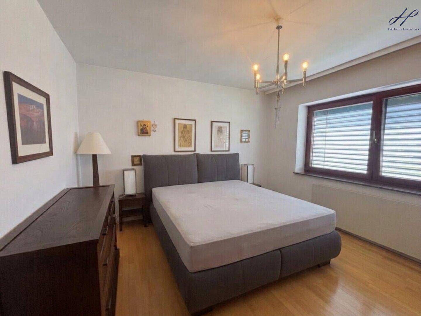 Helles Schlafzimmer mit Doppelbett, Holzboden und Fenster mit Jalousien.