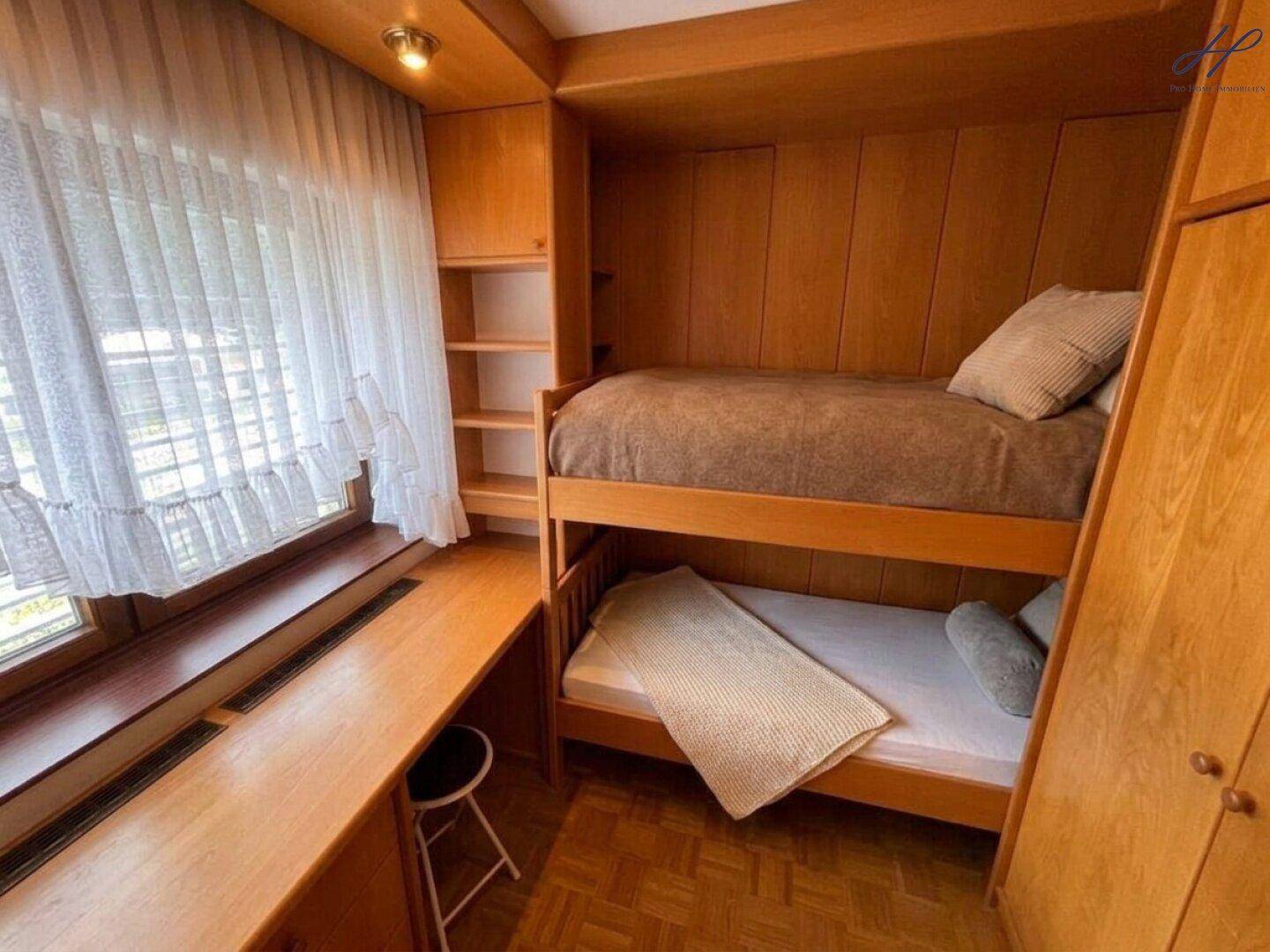 Kinderzimmer mit Etagenbett, Holzeinbauten und Fenster mit Vorhang.
