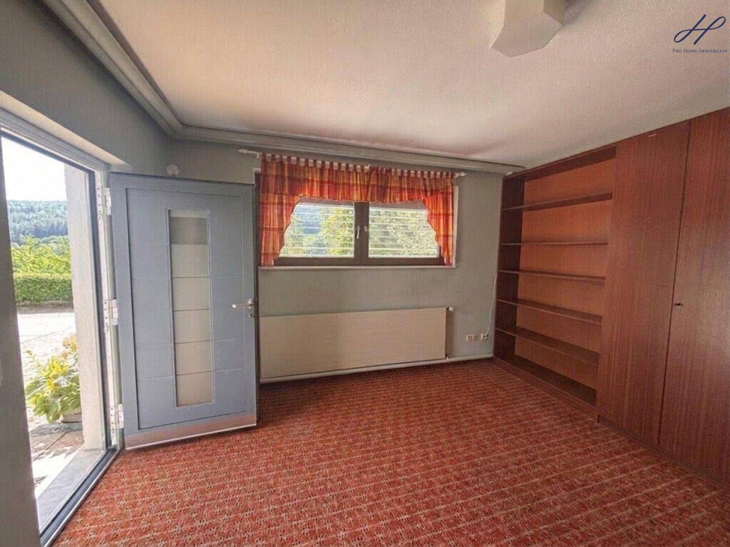 Raum mit Teppichboden, Einbauregalen und Zugang zum Außenbereich.