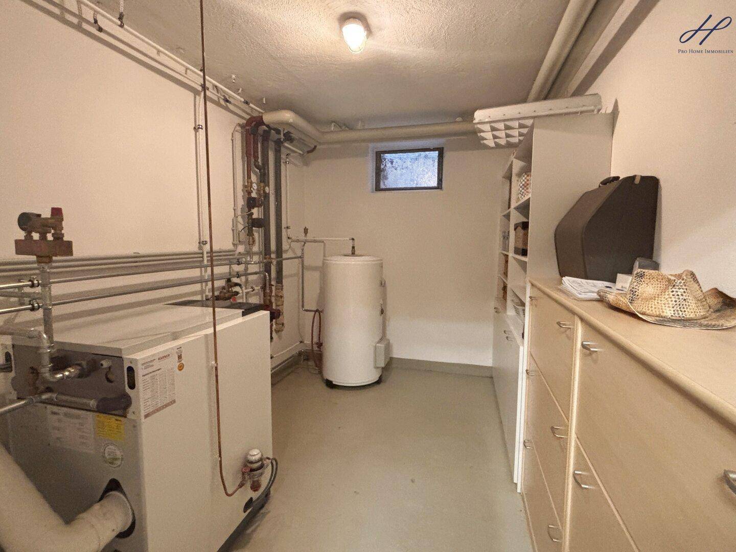 Heizungsraum mit technischen Anlagen, Warmwasserspeicher und kleinem Fenster.