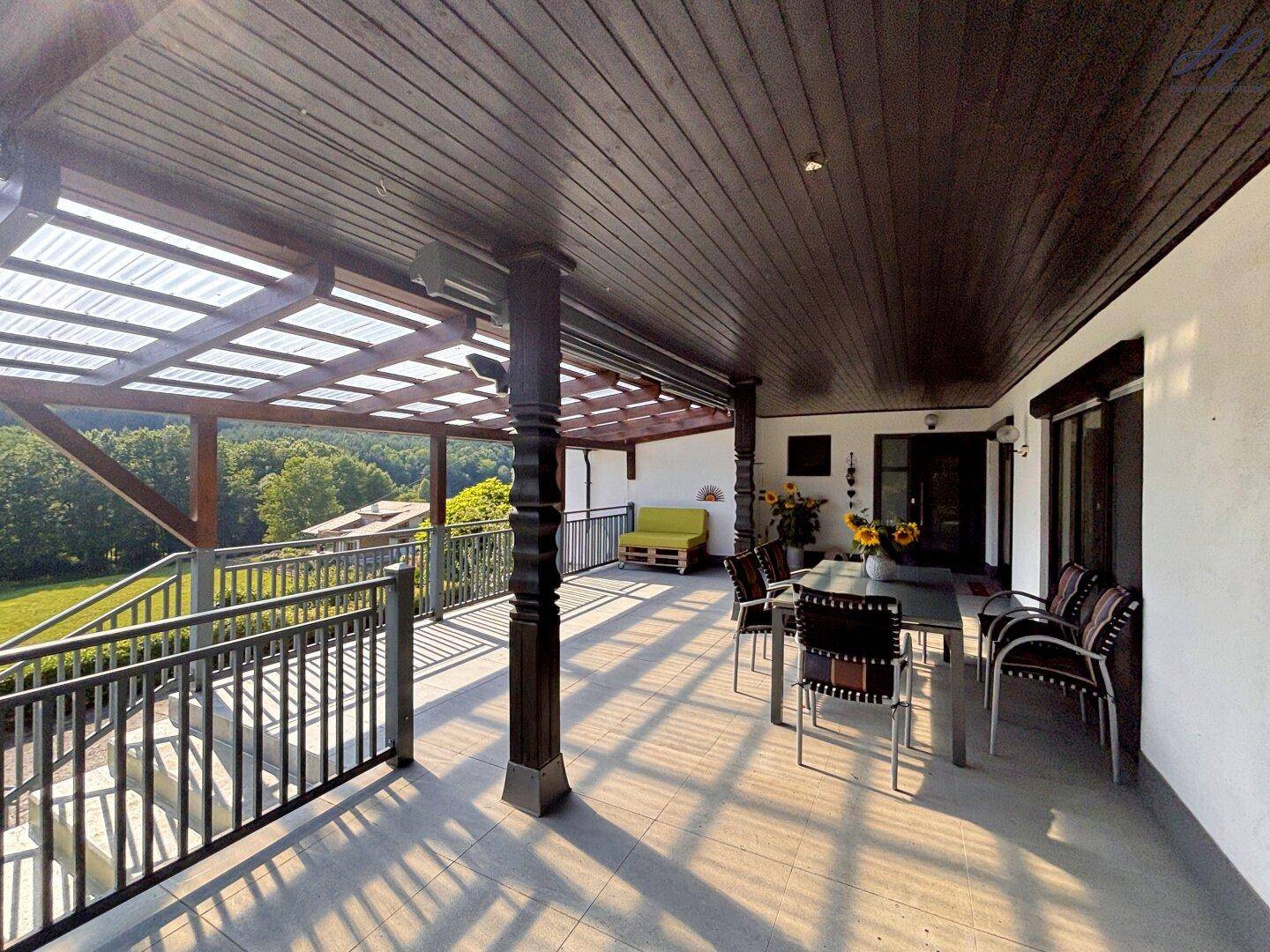 Überdachte Terrasse mit Esstisch, Stühlen und Panoramablick auf die Natur.