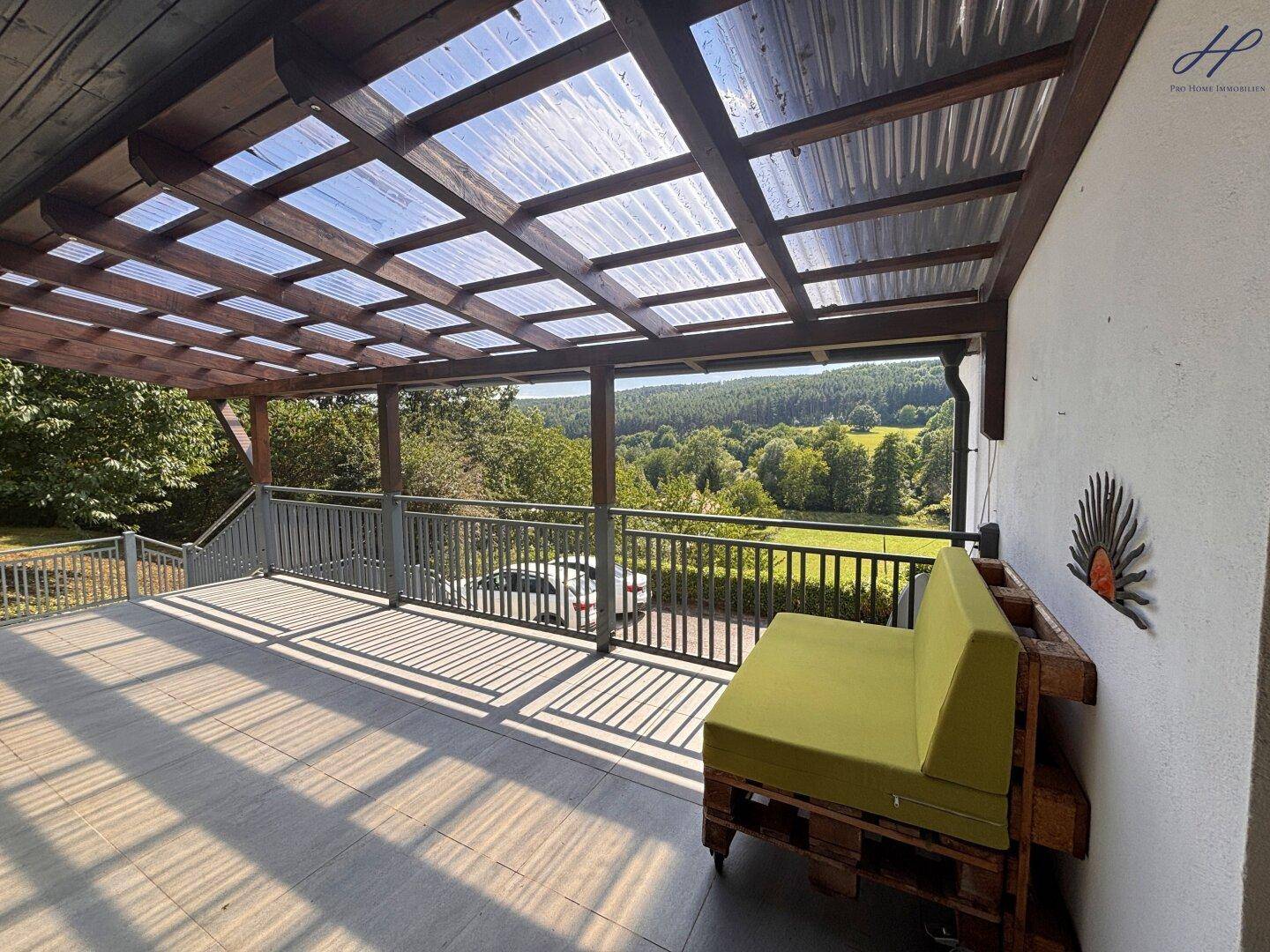 Geräumige überdachte Terrasse mit Palettenmöbeln und weitem Blick über die Landschaft.