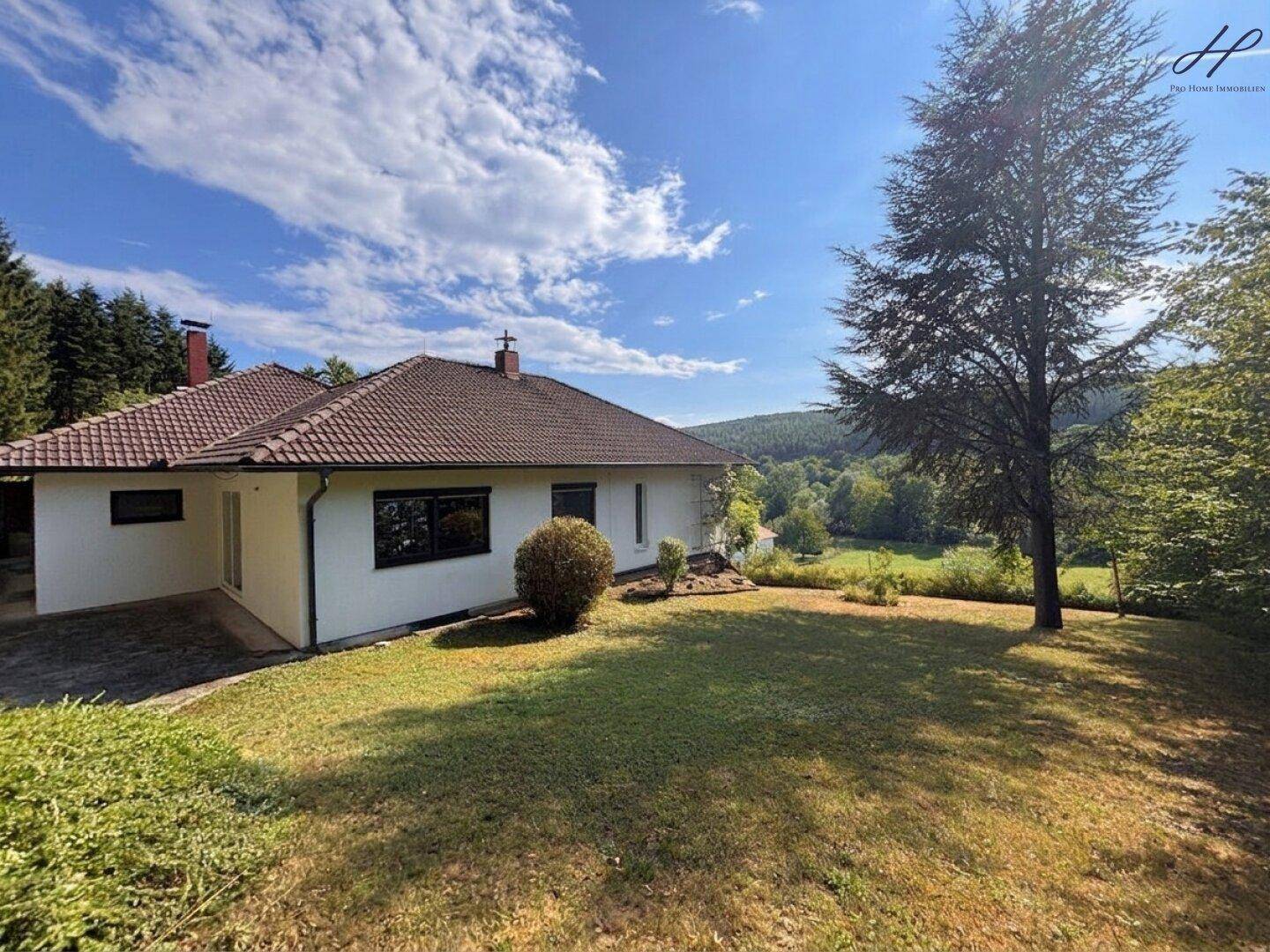 Rückansicht des Hauses mit weitläufigem Rasen und Blick auf die umliegende Hügellandschaft.