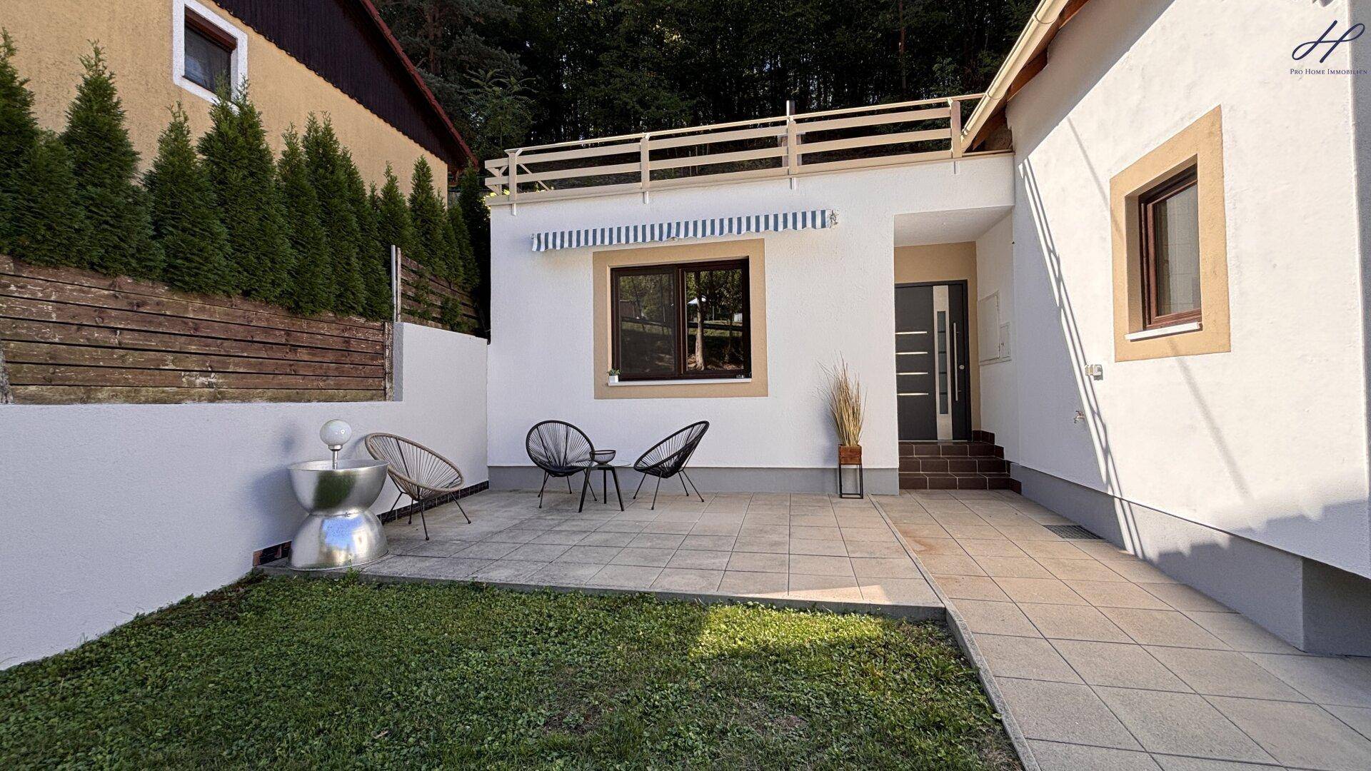 Gemütliche gepflasterte Terrasse mit modernen Gartenmöbeln und kleinem Rasenbereich.