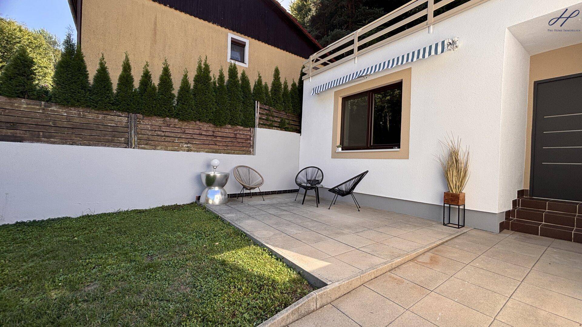 Sonniger Terrassenbereich mit Sitzgelegenheiten und angrenzender Rasenfläche am Haus.