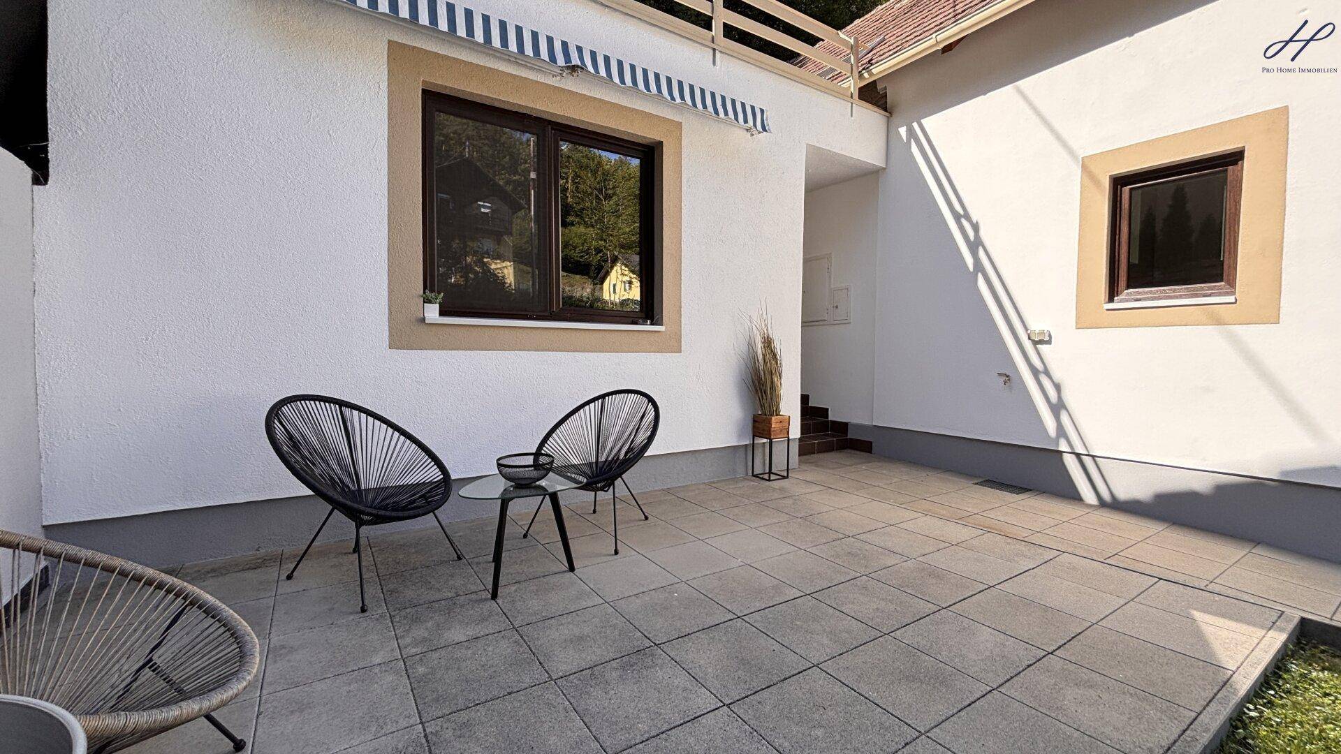 Detailansicht der gepflasterten Terrasse mit zwei modernen Korbsesseln und Beistelltisch.