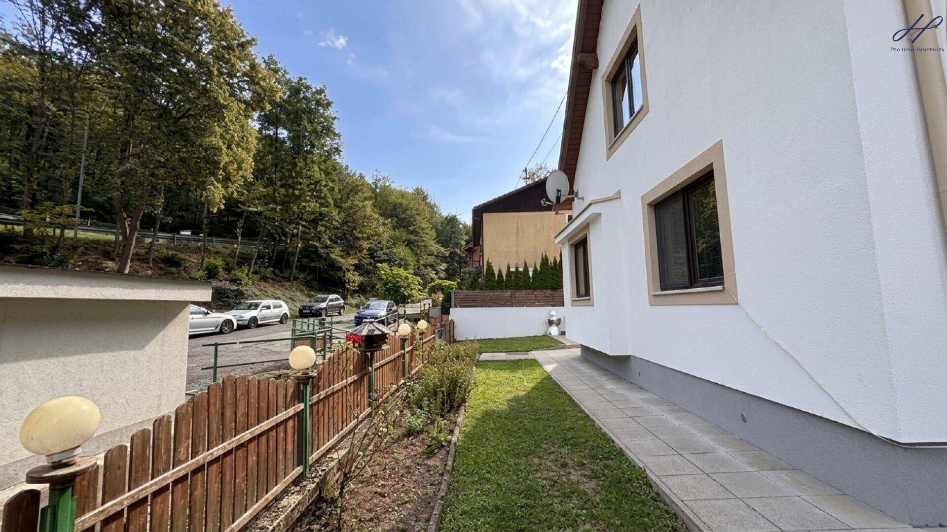 Seitenansicht des Hauses mit gepflegtem Rasenstreifen und Blick auf den Parkplatz.