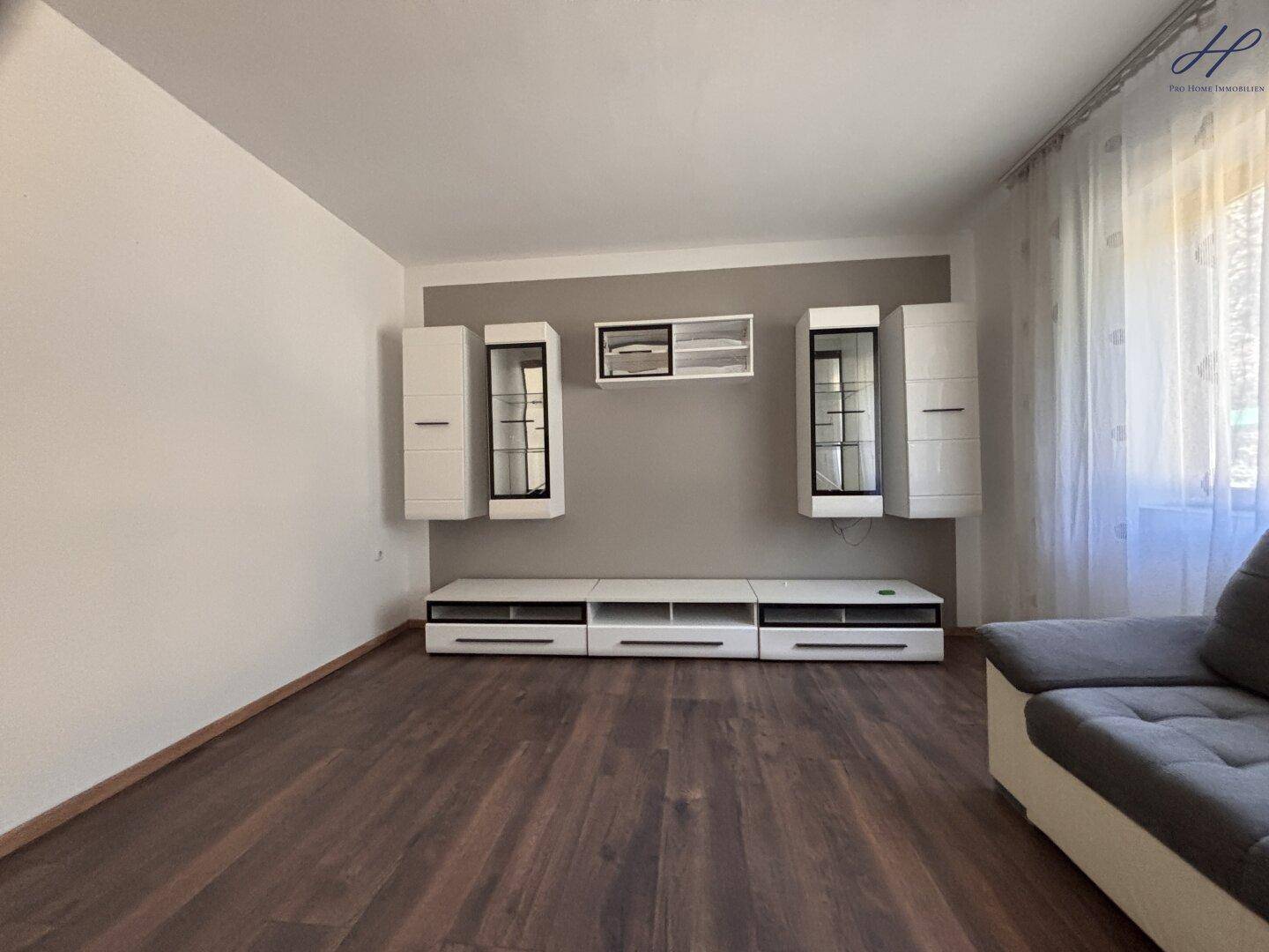 Modern eingerichtetes Wohnzimmer mit Laminatboden, weißer Schrankwand und Sofa.