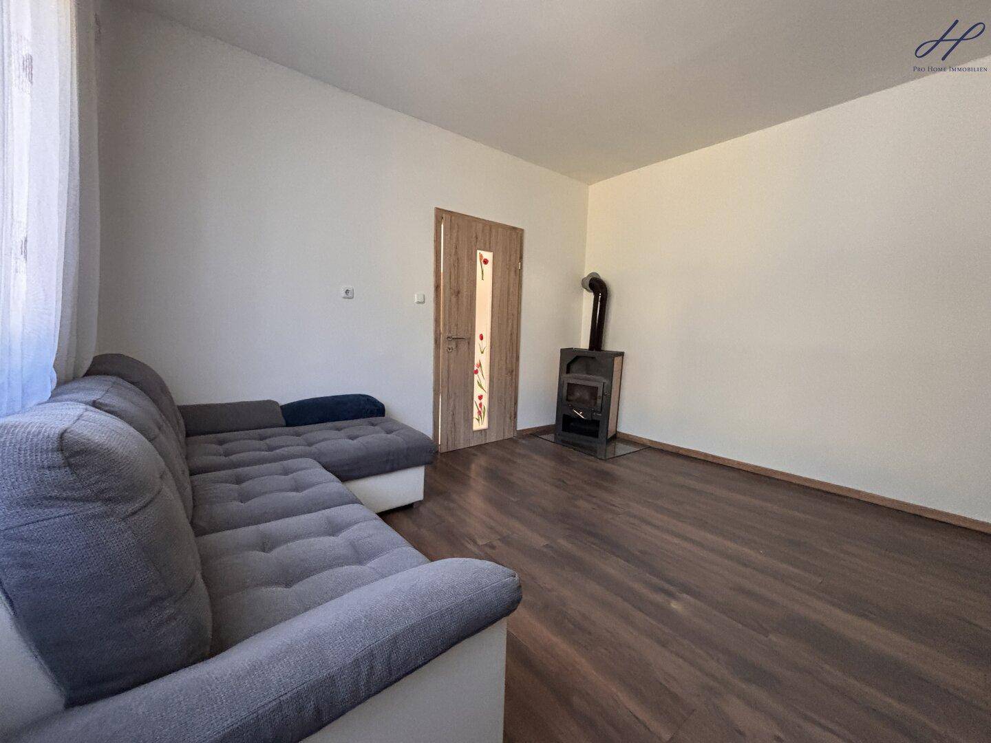 Gemütliches Wohnzimmer mit Laminatboden, Ecksofa und einem Holzofen für Wärme.