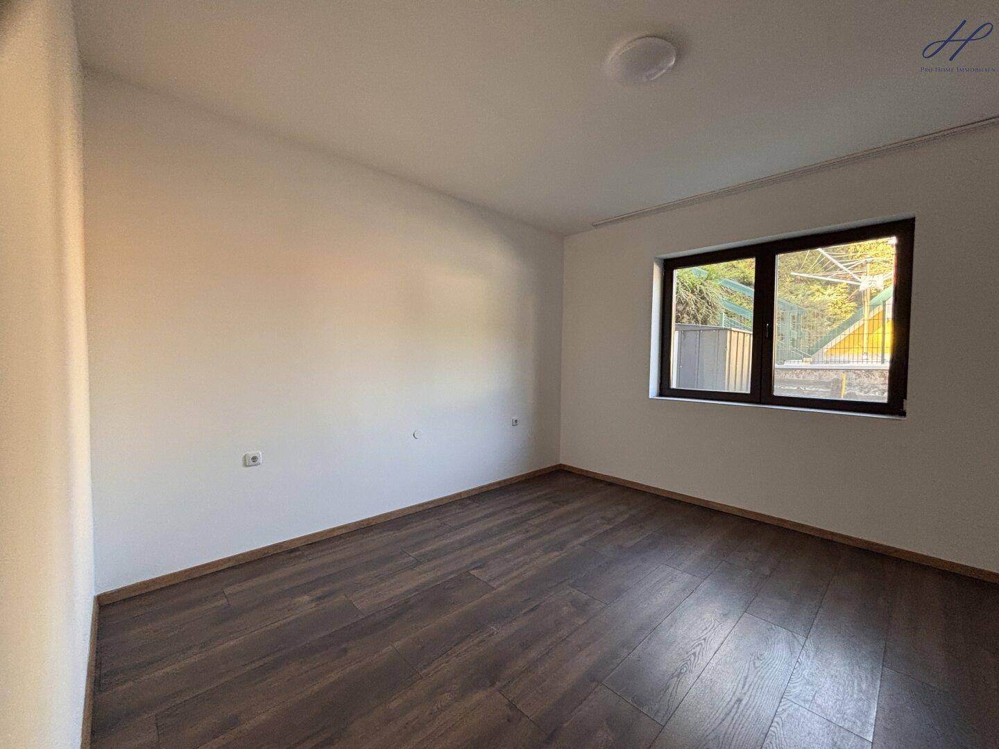 Helles Schlafzimmer mit Laminatboden und Fenster, das viel Tageslicht hereinlässt.