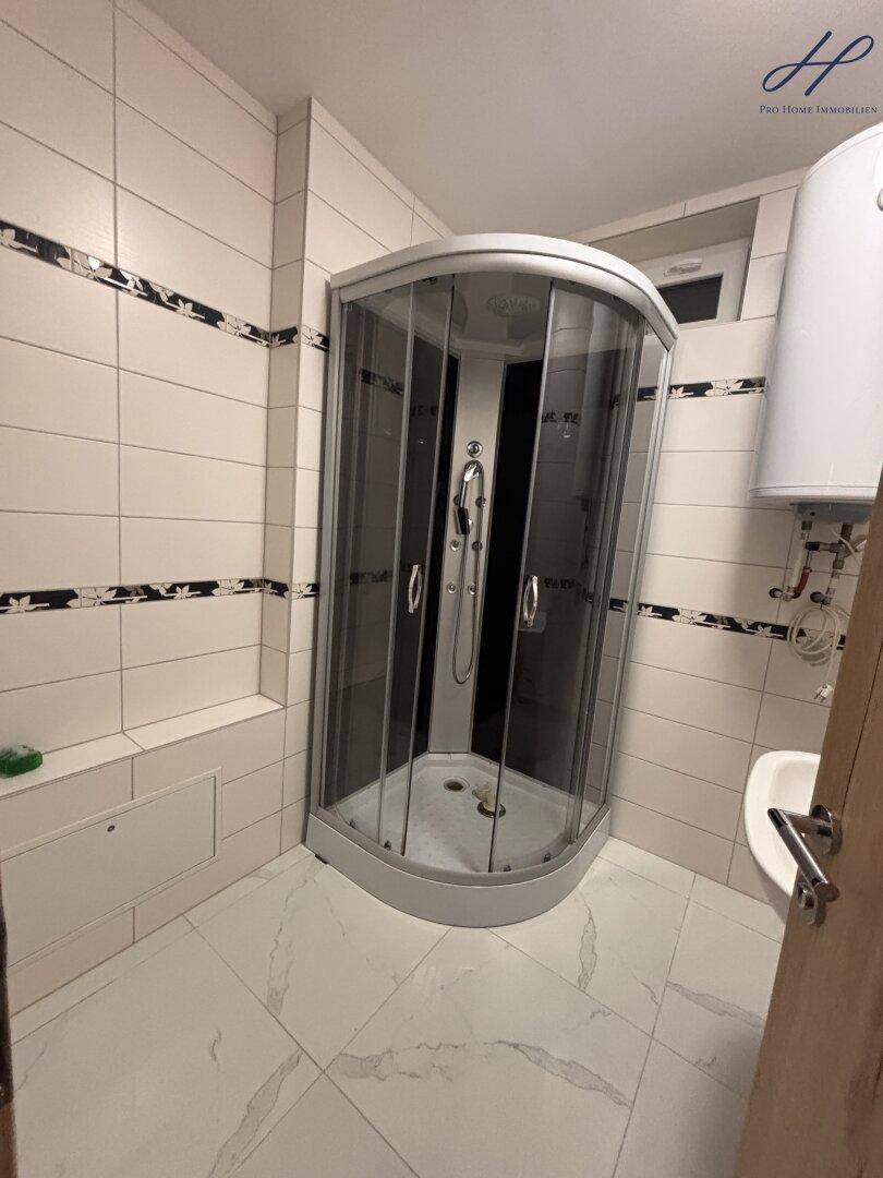 Modern gefliestes Badezimmer mit Duschkabine, weißem Waschbecken und Boiler.