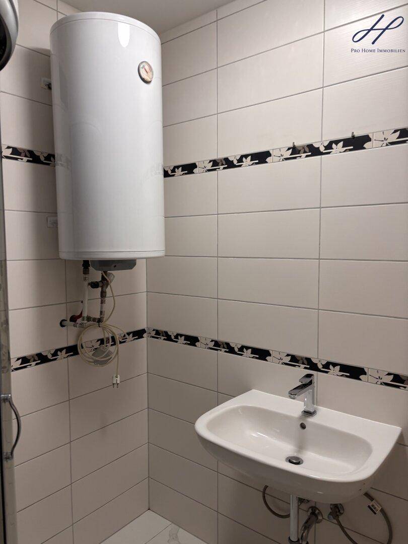Badezimmer mit weißem Waschbecken, Wandfliesen und einem Warmwasserboiler.