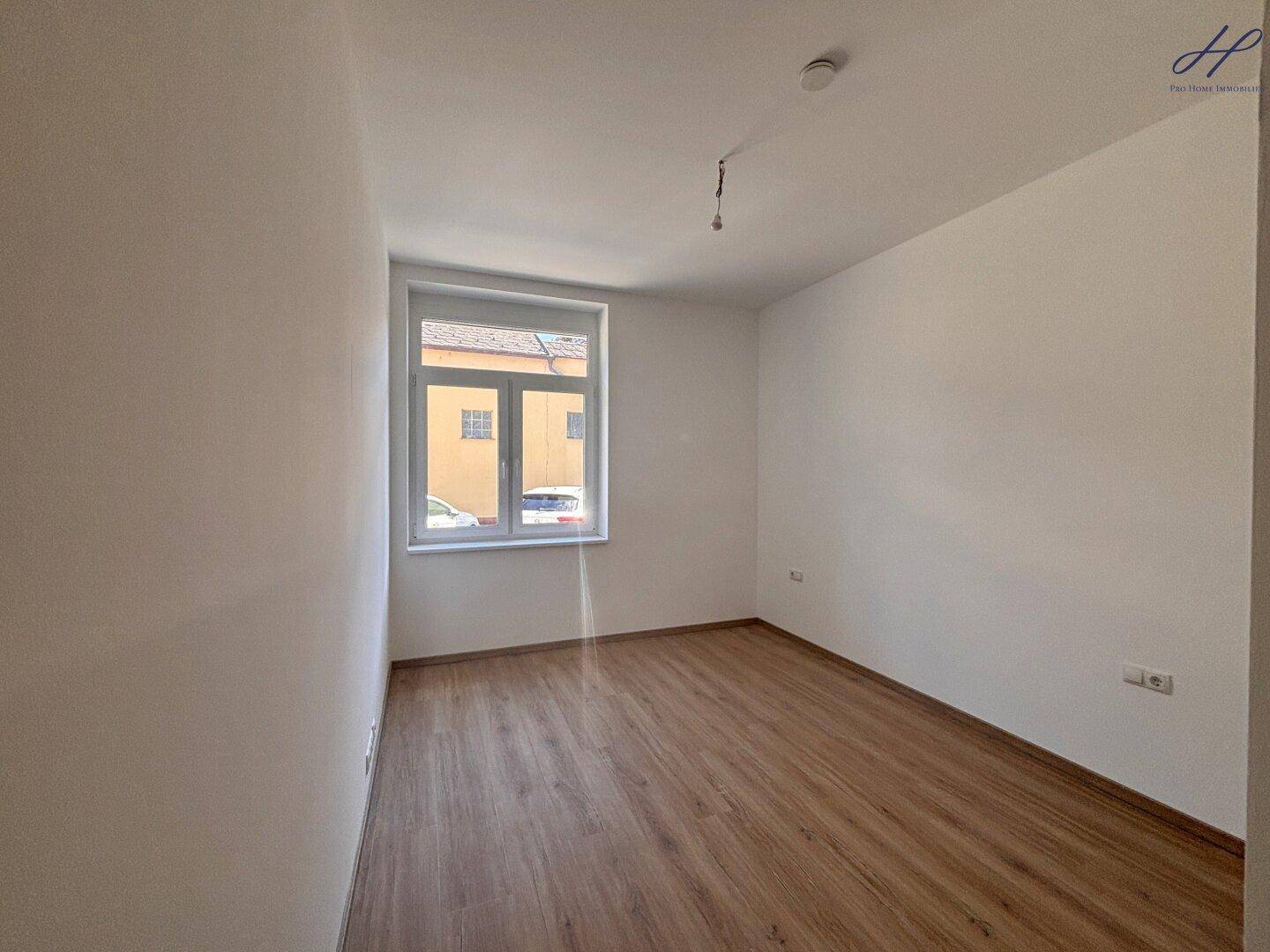 Helles Schlafzimmer mit Vinylboden und großem Fenster, das viel Tageslicht hereinlässt.