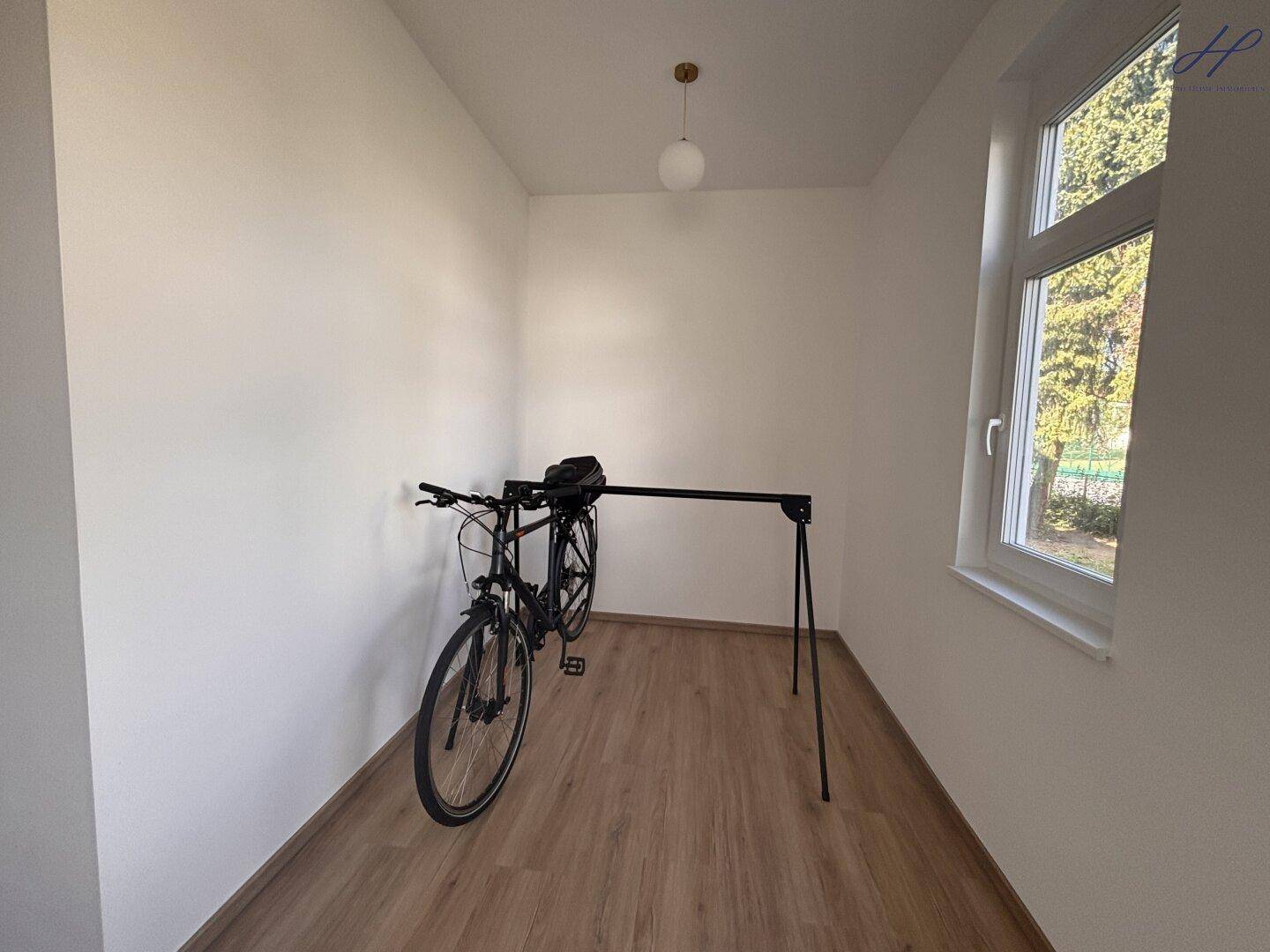 Heller Raum mit Vinylboden und Fenster, derzeit als Fahrradabstellraum genutzt.
