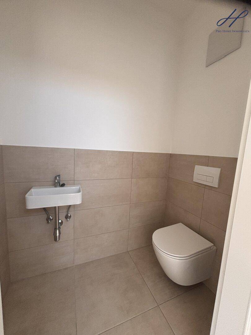Modernes Gäste-WC mit beigefarbenen Fliesen, wandhängendem WC und kleinem Waschbecken.
