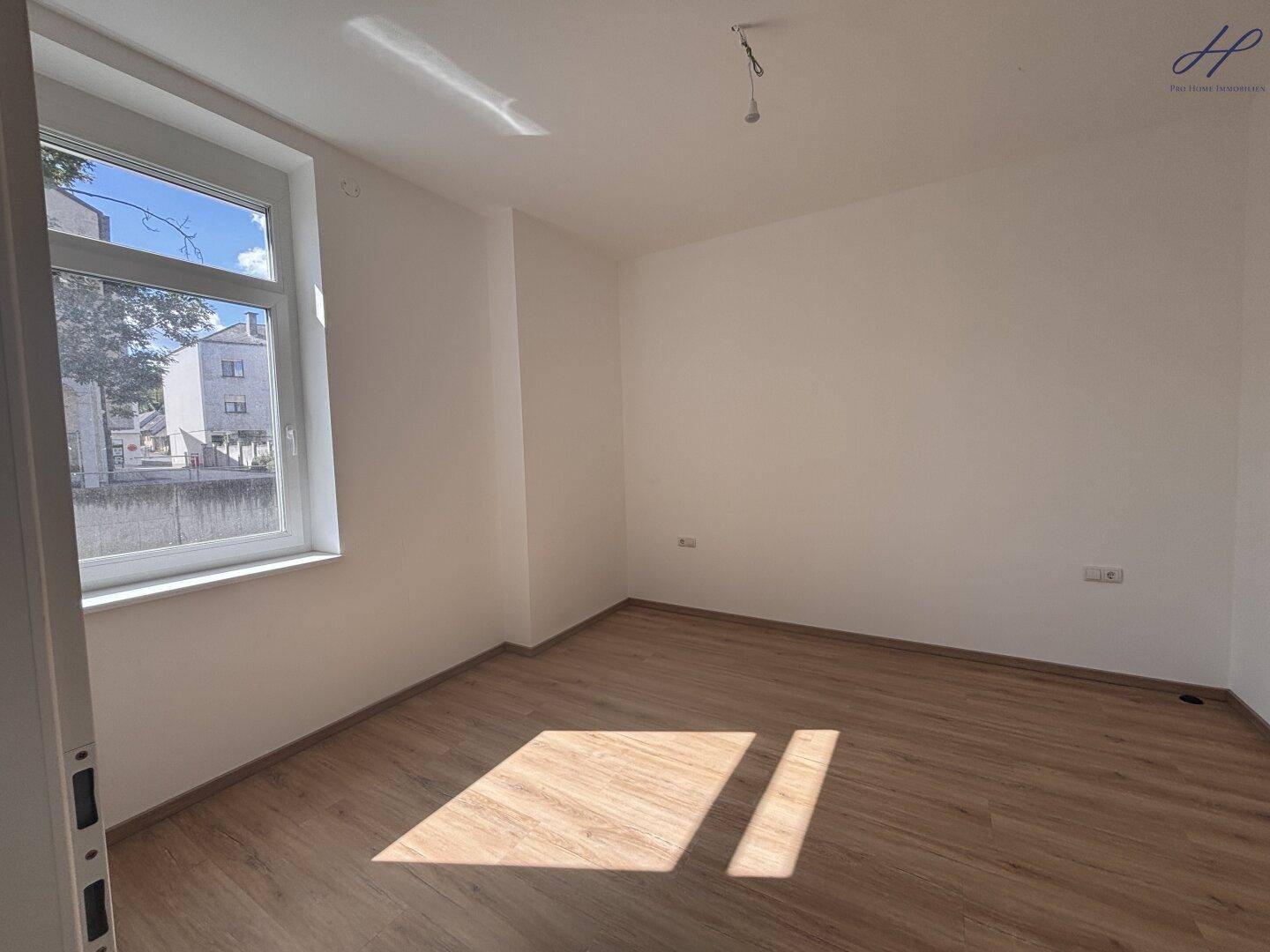 Helles Schlafzimmer mit Laminatboden und einem großen Fenster, das viel Tageslicht hereinlässt.