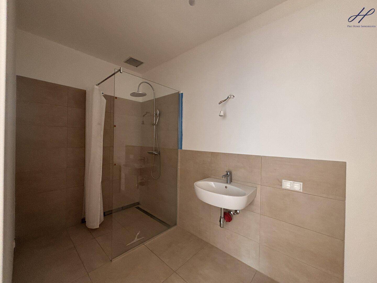 Modernes Badezimmer mit ebenerdiger Dusche, beigefarbenen Fliesen und kleinem Waschbecken.