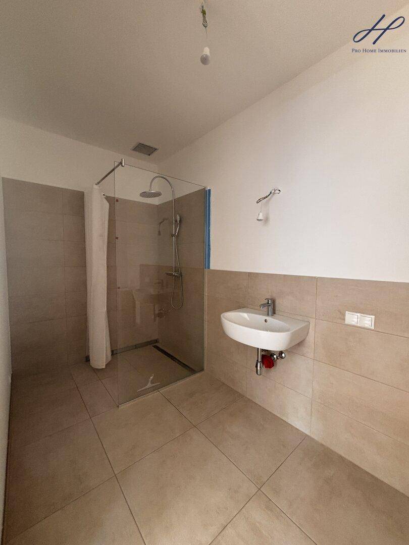 Modernes Badezimmer mit ebenerdiger Dusche, beigefarbenen Fliesen und kleinem Waschbecken.