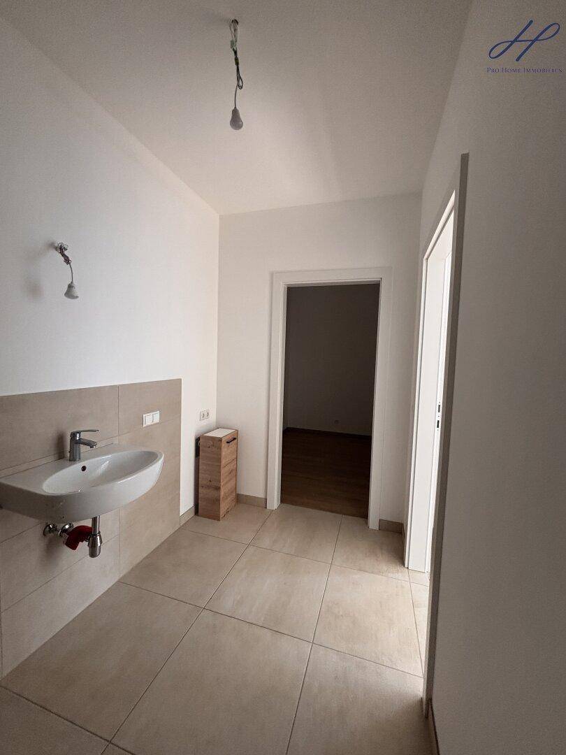 Helles Badezimmer mit beigefarbenen Fliesen, Waschbecken und Zugang zu einem weiteren Raum.