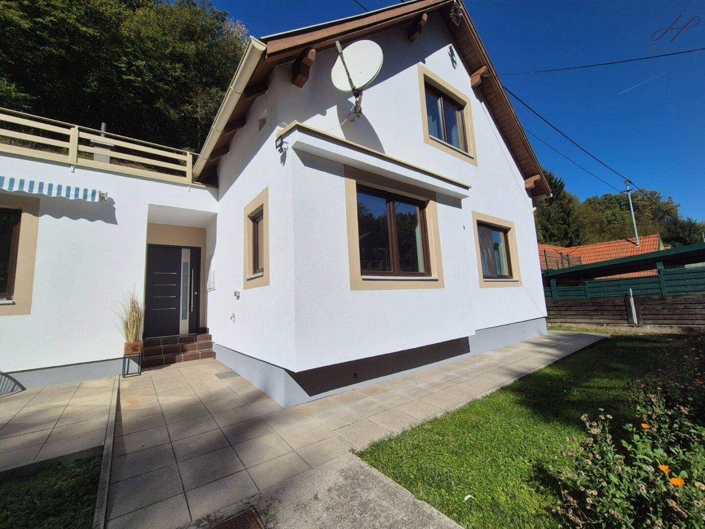 Ansicht des weißen Einfamilienhauses mit braunen Fensterrahmen und Eingangsbereich.