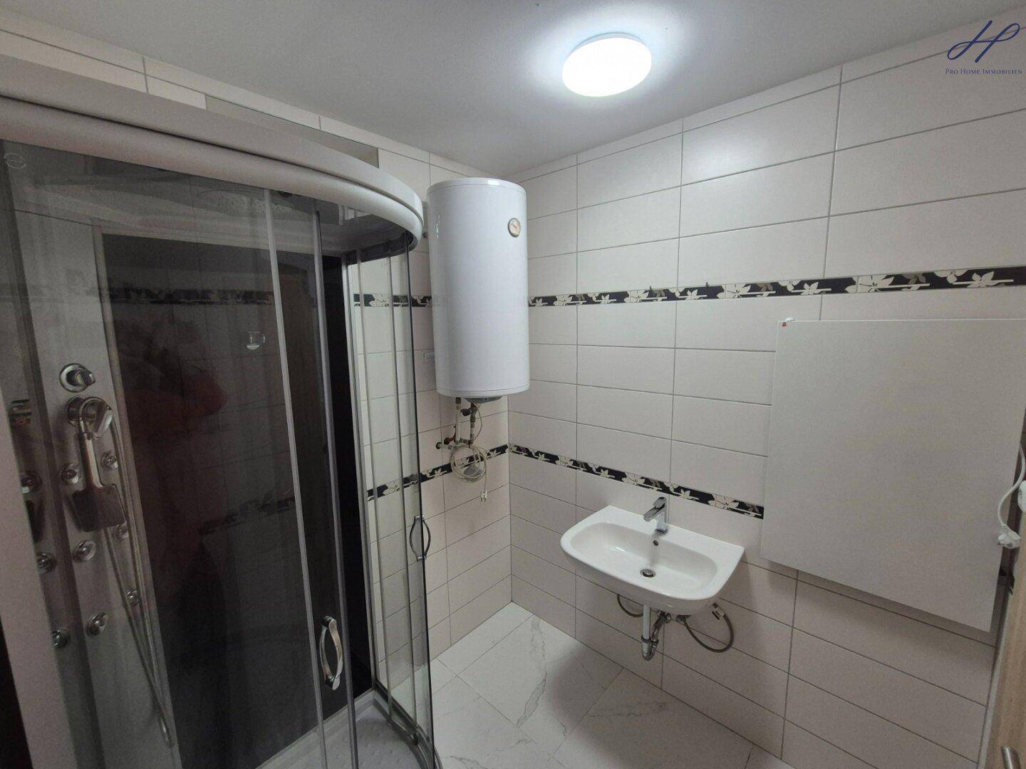 Modern gefliestes Badezimmer mit Duschkabine, Waschbecken und weißem Warmwasserboiler.