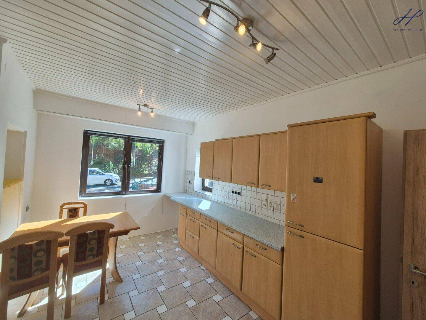 Funktionale Küche mit hellen Holzschränken, gefliestem Boden und einem kleinen Essbereich am Fenster.