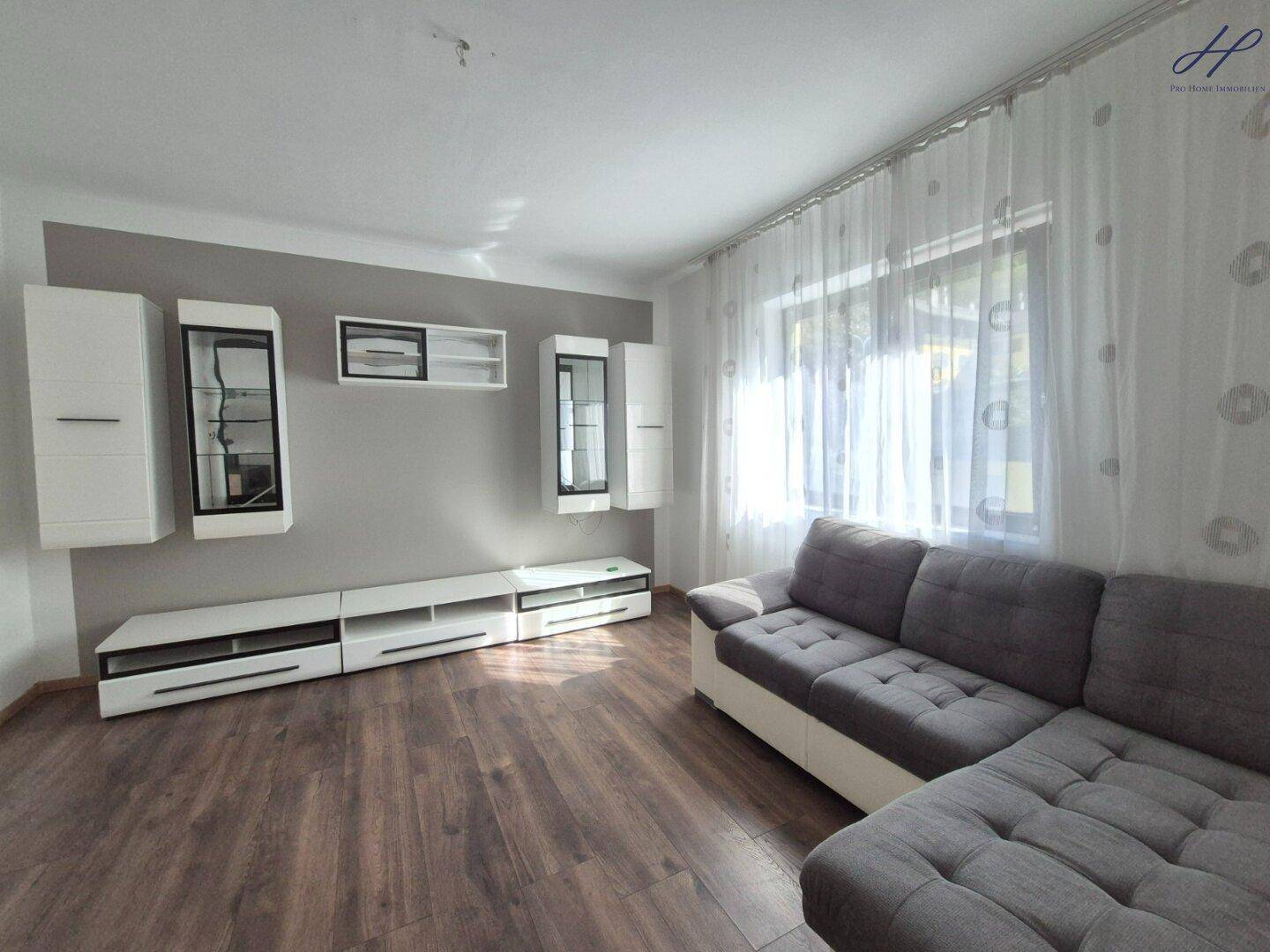 Helles Wohnzimmer mit modernem Laminatboden, bequemer grauer Couch und weißen Wandregalen.