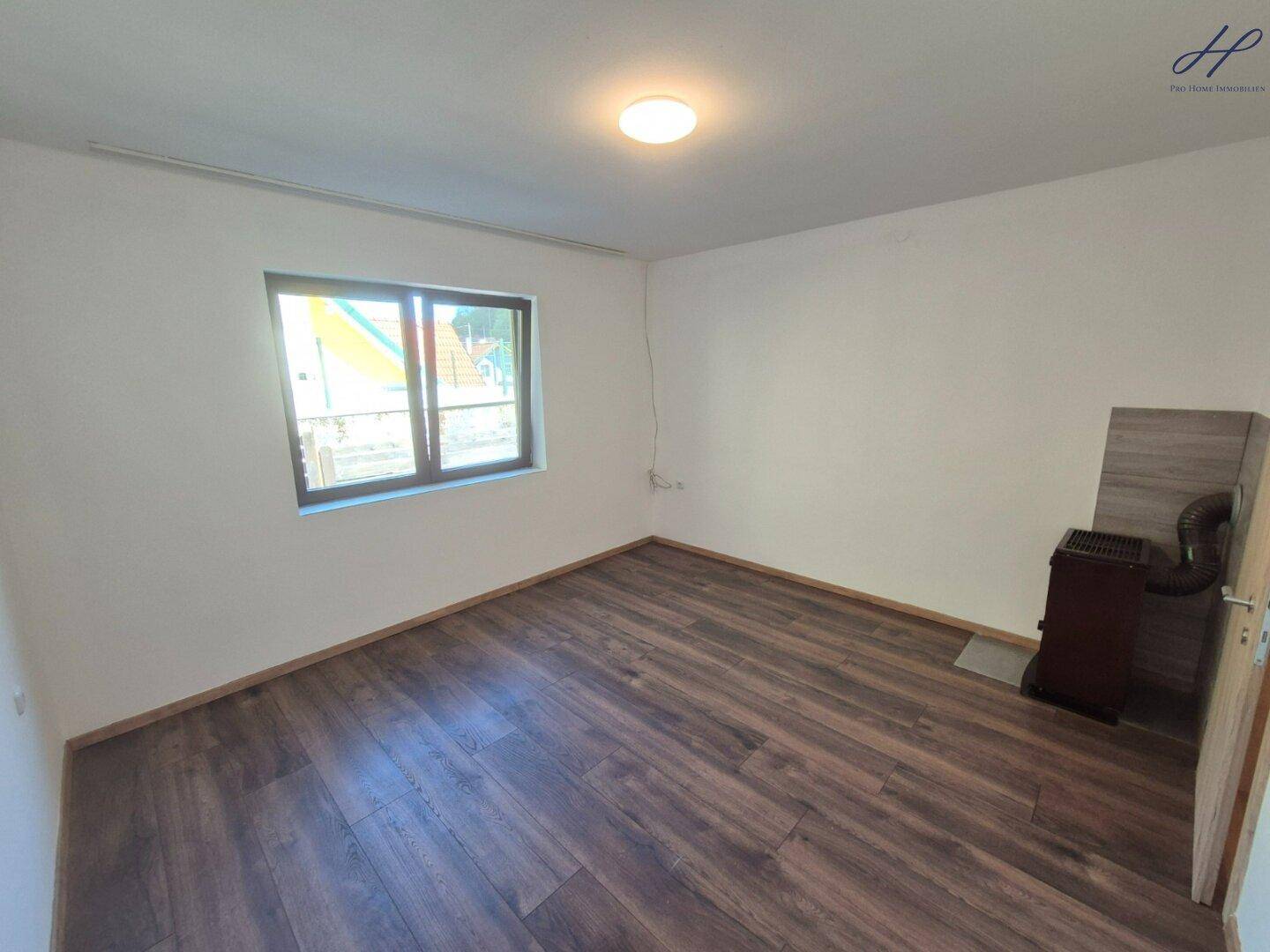 Leeres Schlafzimmer mit dunklem Laminatboden, weißen Wänden und einem kleinen Ofen in der Ecke.