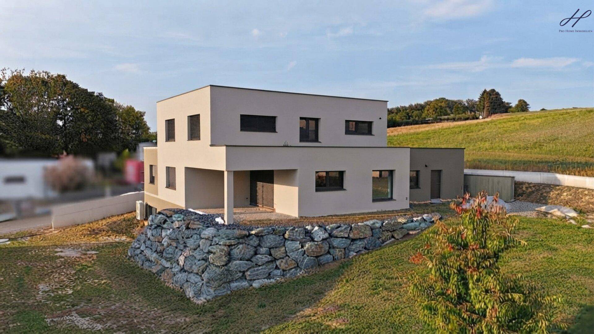 Ansicht des modernen Hauses mit beiger Fassade, umgeben von grüner Landschaft und einem Steingarten.