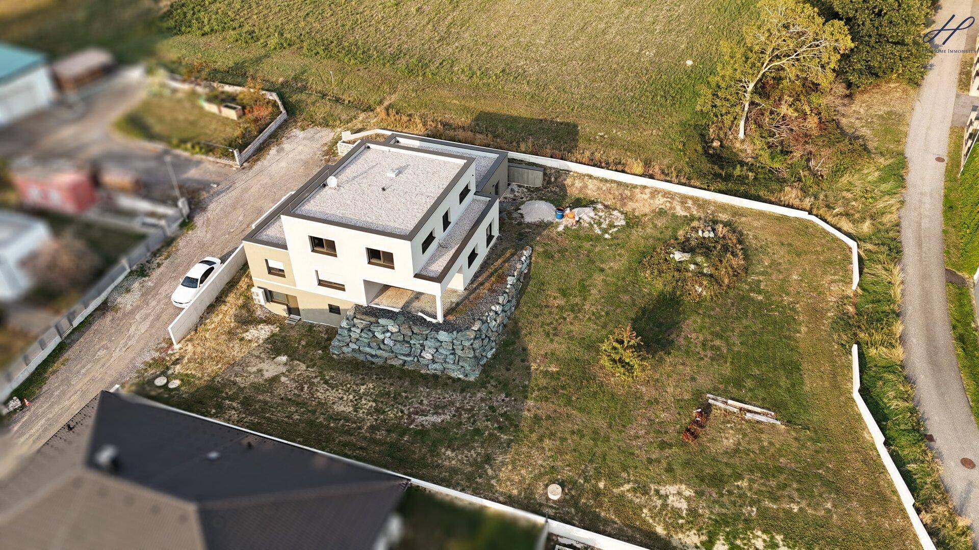 Luftaufnahme des modernen Hauses mit Flachdach, großem Grundstück und angrenzender Zufahrt.