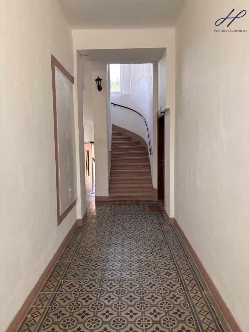 Heller Flur mit gemusterten Fliesen und einer geschwungenen Treppe im Hintergrund.