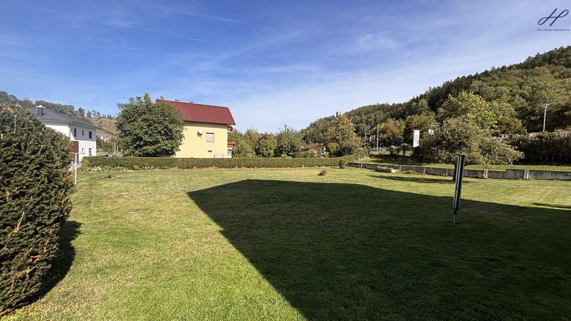 Weitläufige Rasenfläche des Gartens mit Blick auf die umliegenden Häuser und die grüne Hügellandschaft.