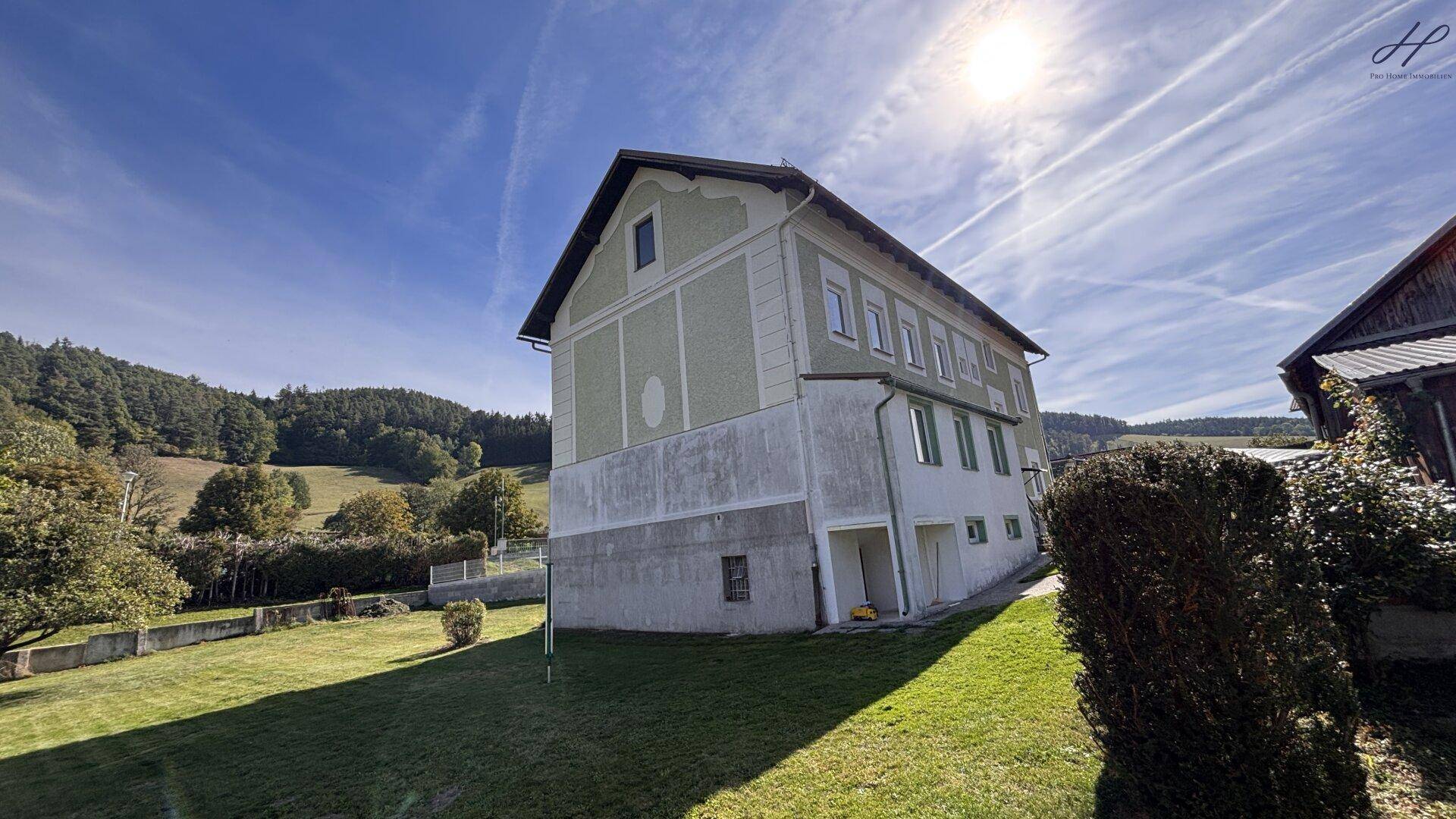 Rückwärtige Seitenansicht des Hauses vom Garten aus, mit weitem Blick über die grüne Landschaft.