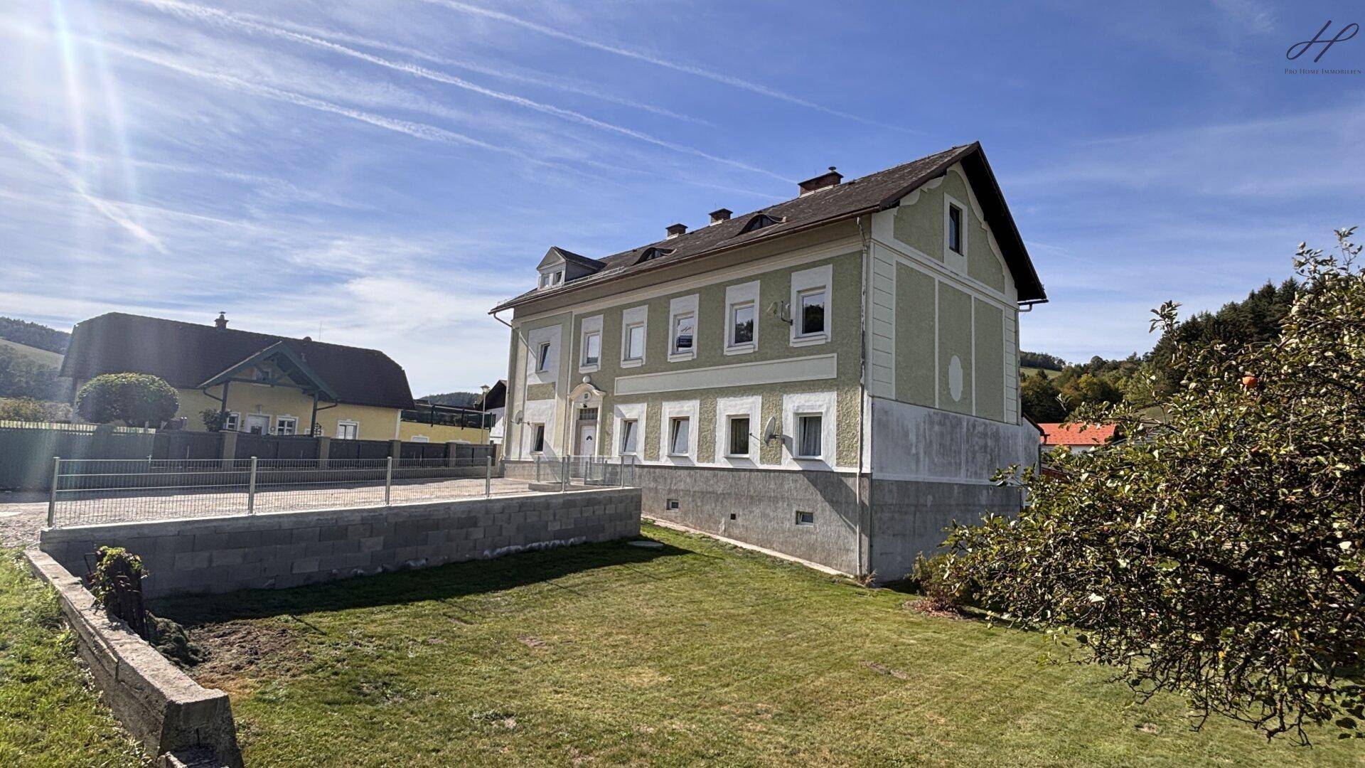 Seitenansicht des Hauses vom Garten aus, mit einer großen Rasenfläche und sonnigem Wetter.
