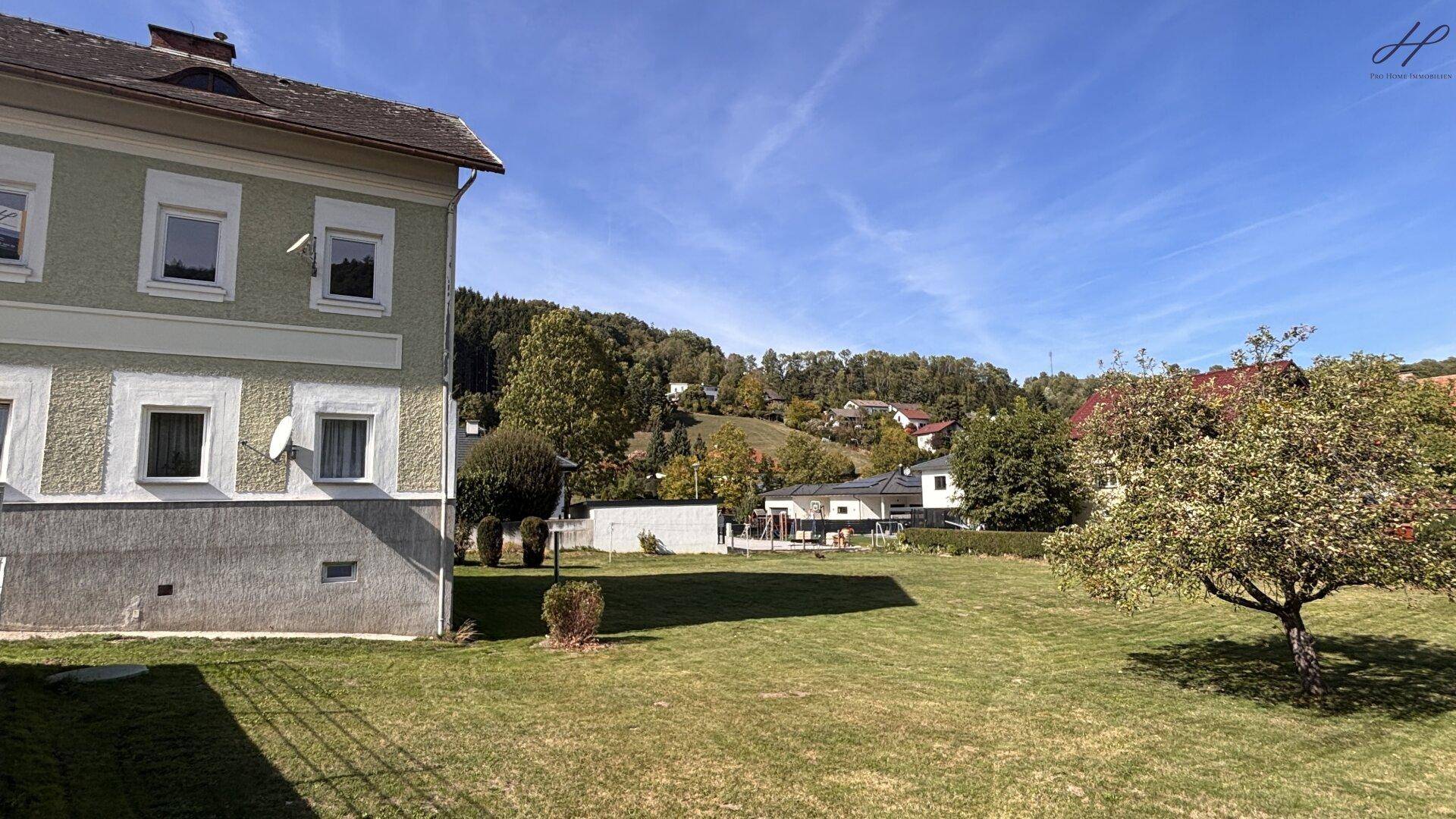 Ansicht des Hauses vom Garten aus, mit einer gepflegten Rasenfläche und Blick auf die grüne Umgebung.