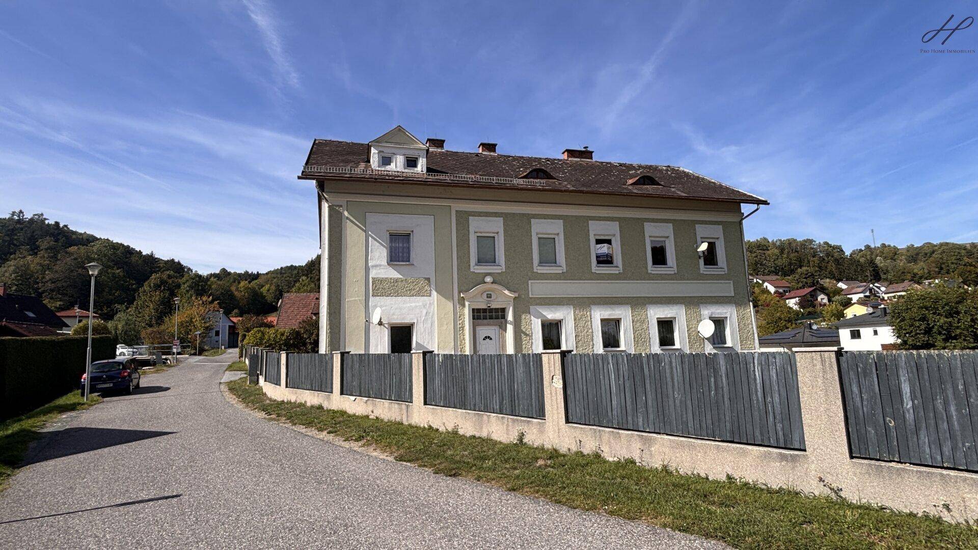 Ansicht des Hauses von der Straße aus, mit einem Holzzaun und der ländlichen Umgebung im Hintergrund.