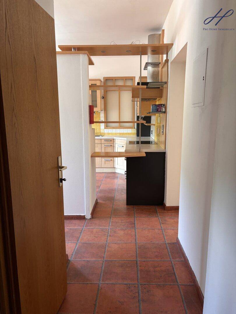 Blick vom Flur in die Küche mit Terrakotta-Fliesenboden und Holzelementen.