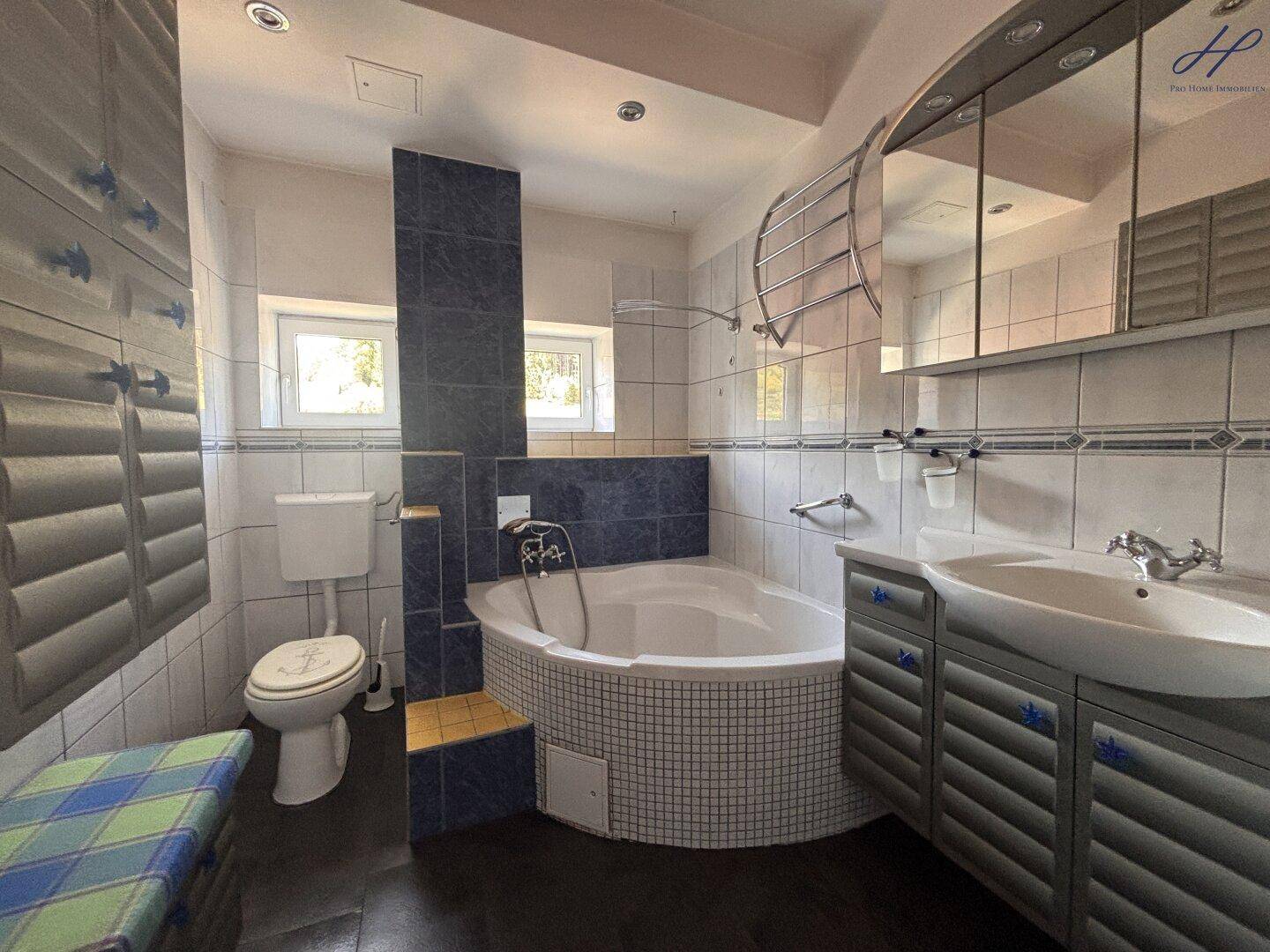 Badezimmer mit Eckbadewanne, blauen und weißen Fliesen sowie einem Waschtisch mit Spiegelschrank.