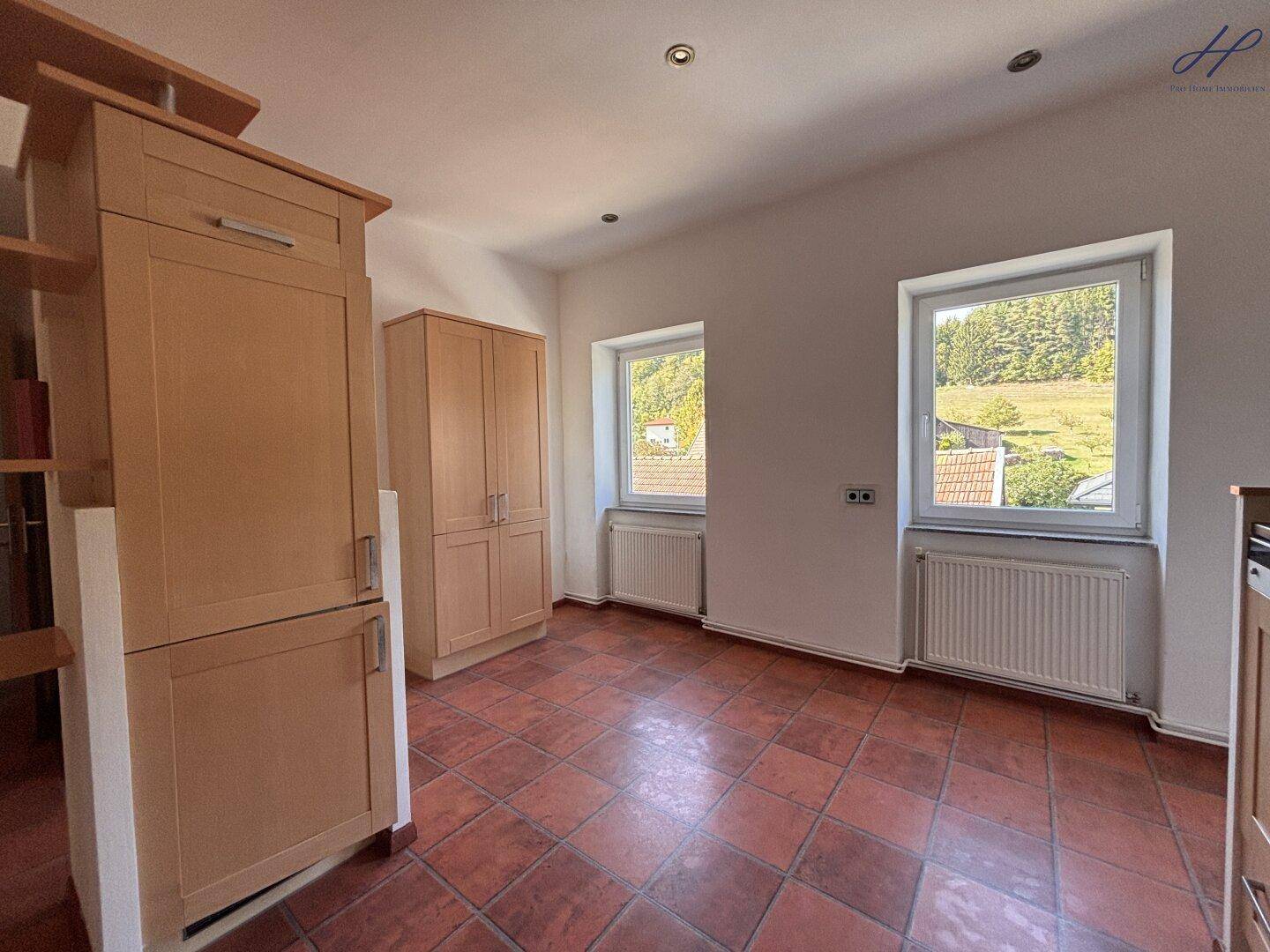 Heller Raum mit Terrakotta-Fliesenboden und zwei Fenstern, die viel Tageslicht hereinlassen.