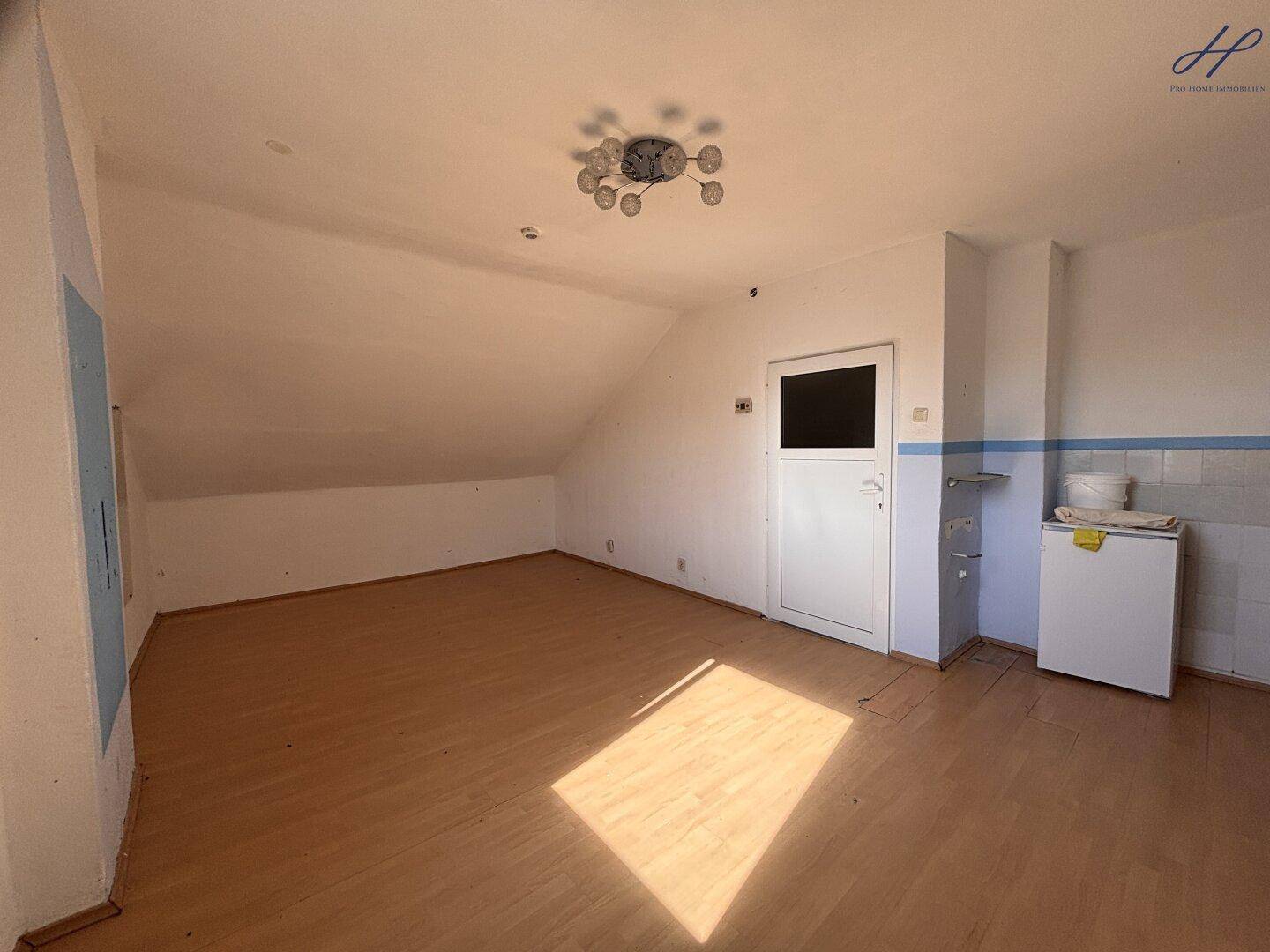 Dachgeschossraum mit schrägen Decken, Laminatboden und einem kleinen Gefrierschrank.