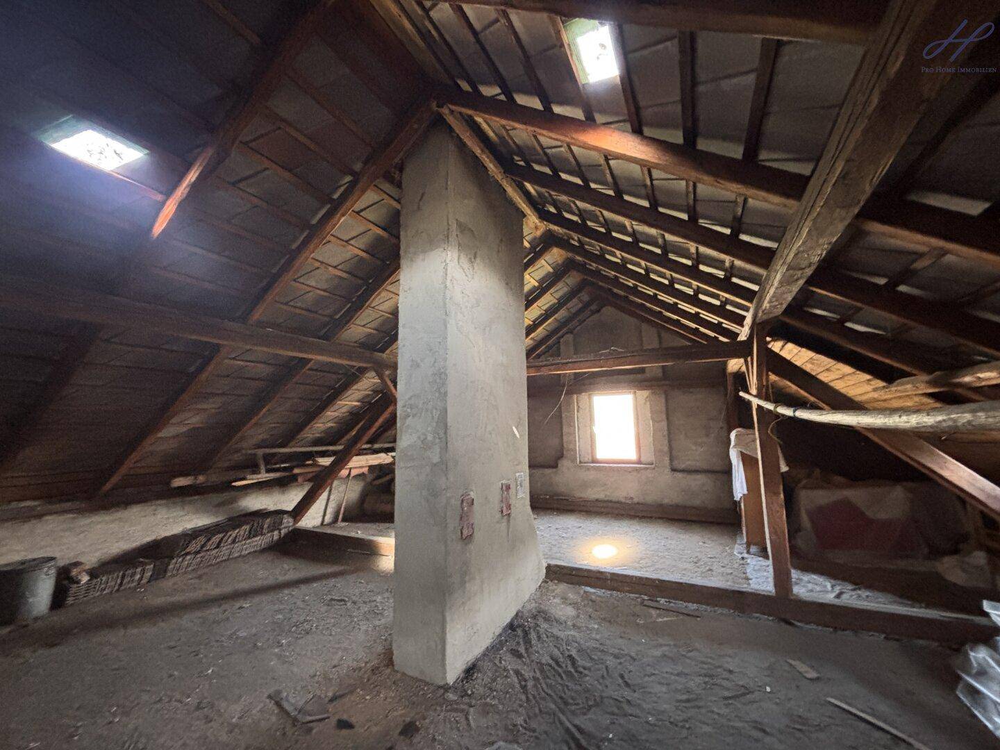 Unausgebauter Dachboden mit sichtbaren Holzbalken und einem Schornstein, bietet Ausbaupotenzial.